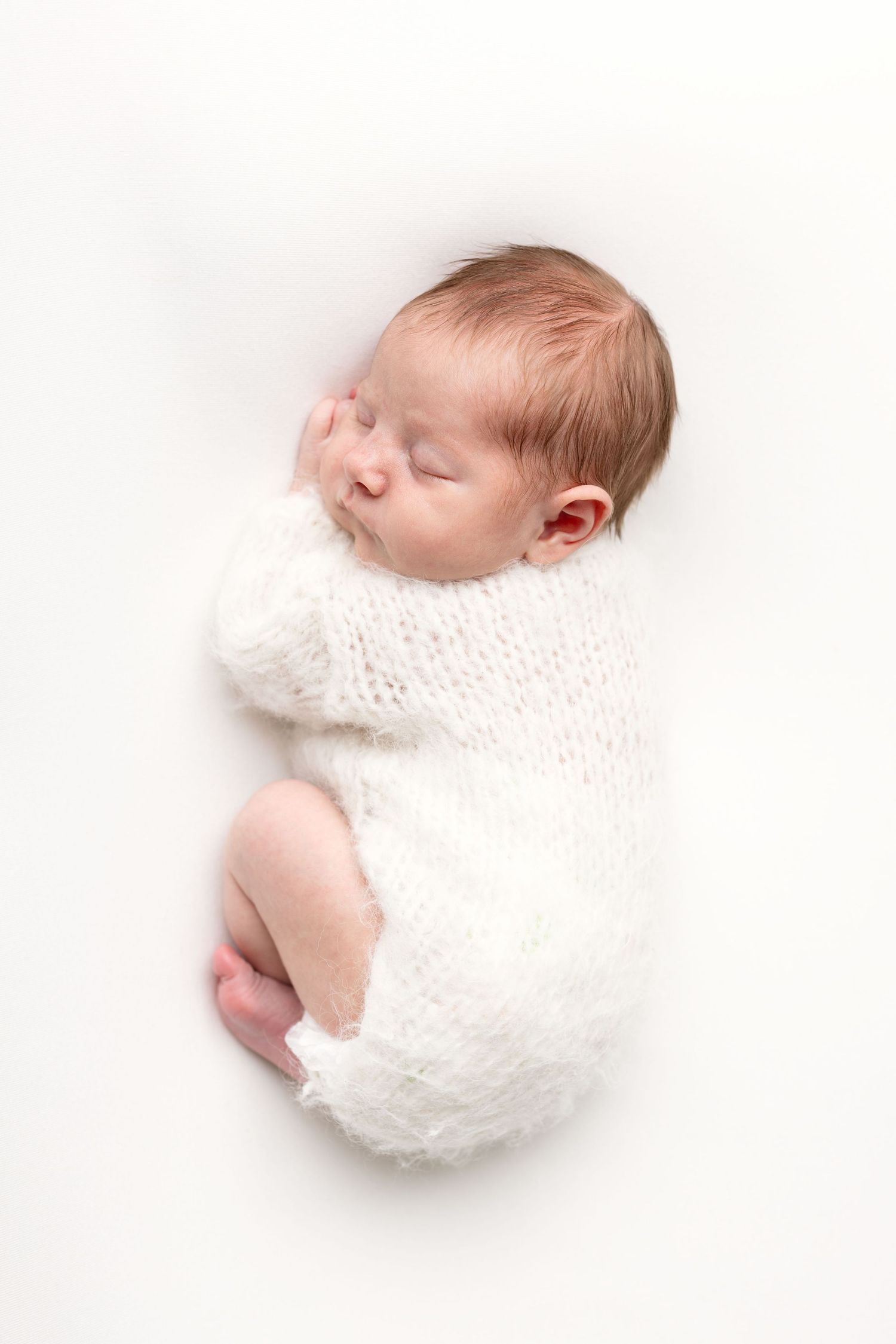 Sleeping newborn baby wrapped in a soft white knit blanket on a white background.