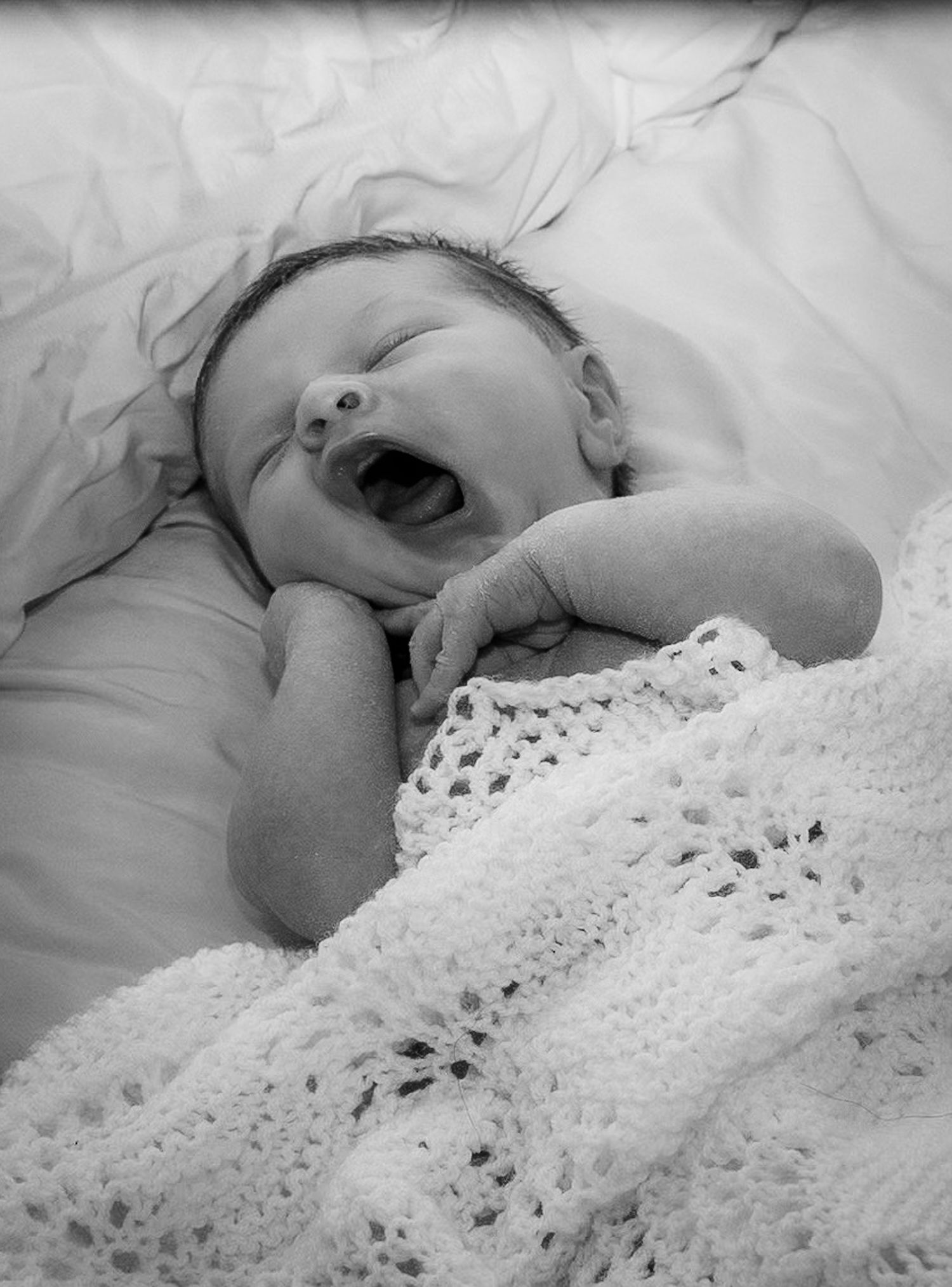 newborn baby pictured yawning whilst relaxing in their parent's bed.