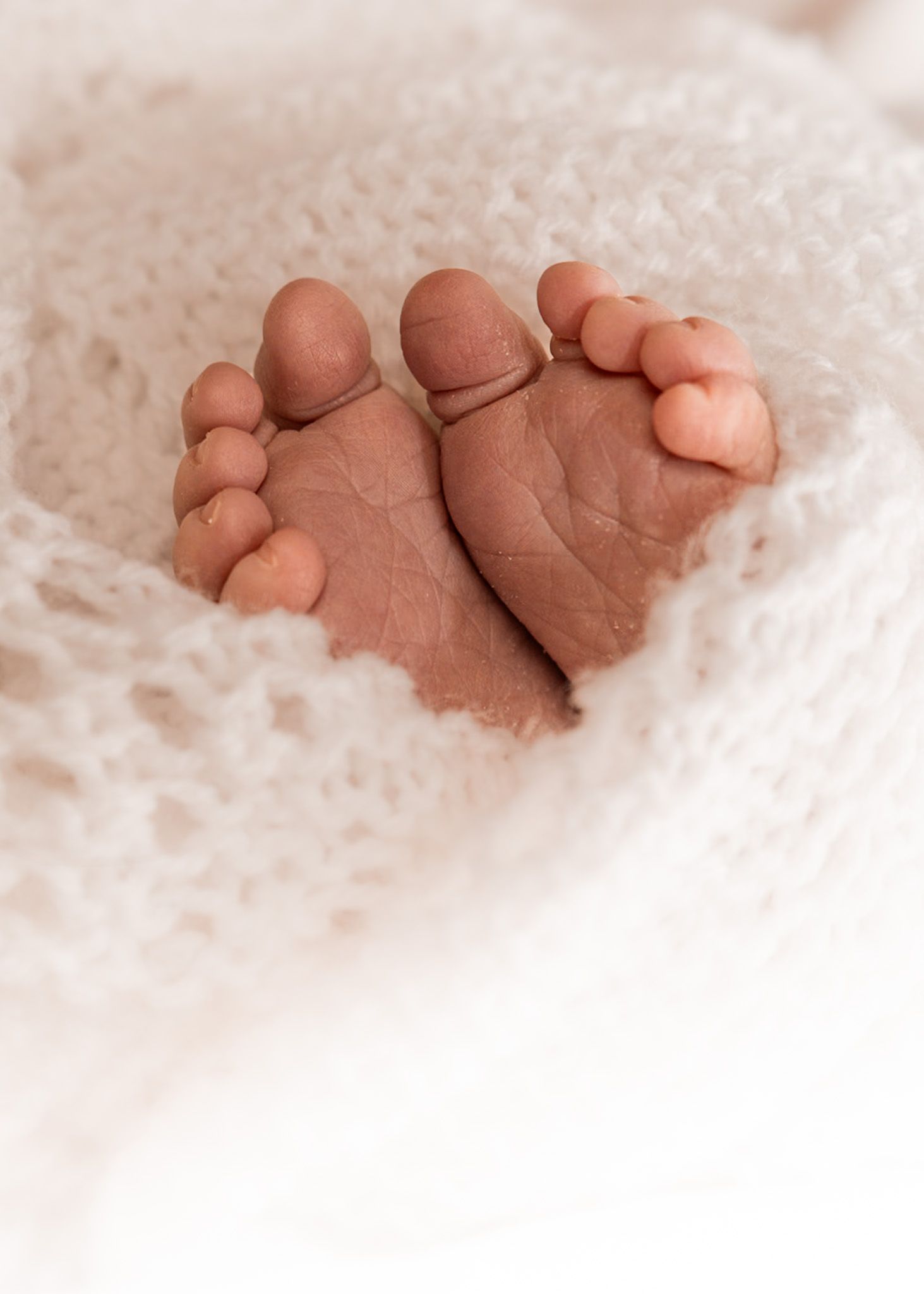 Close up photograph of newborn baby's feet wrapped in a hand-knitted white shawl.