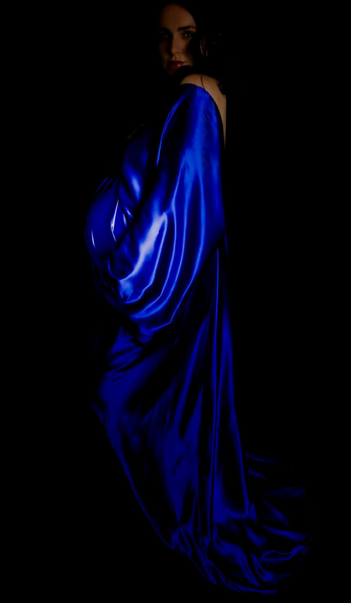 studio maternity photo, mum-to-be's side profile photographed in a blue dress, holding baby bump from below.