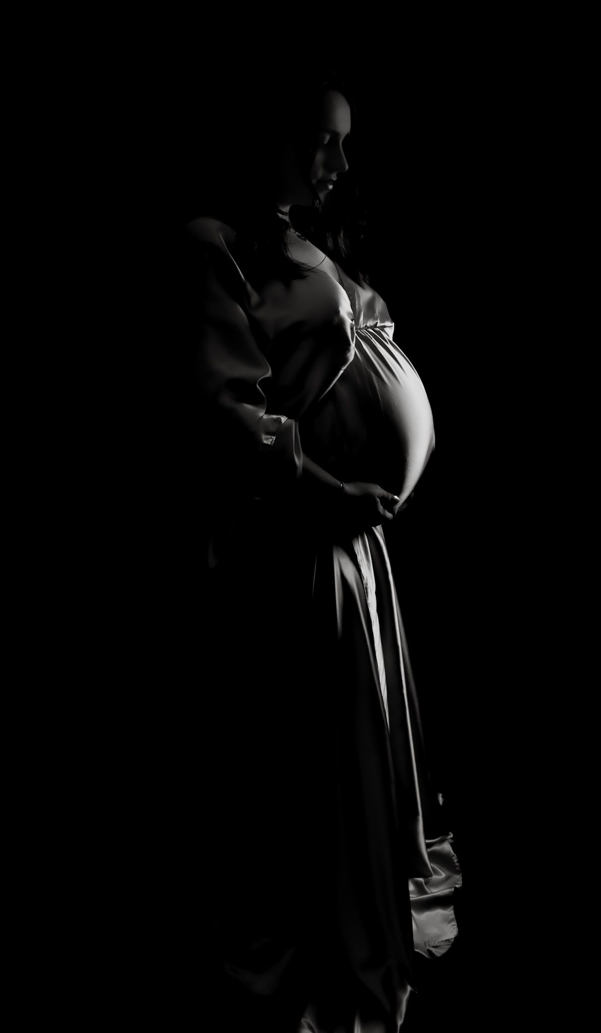 studio maternity photo, mum-to-be photographed in a long dress looking down at bump.