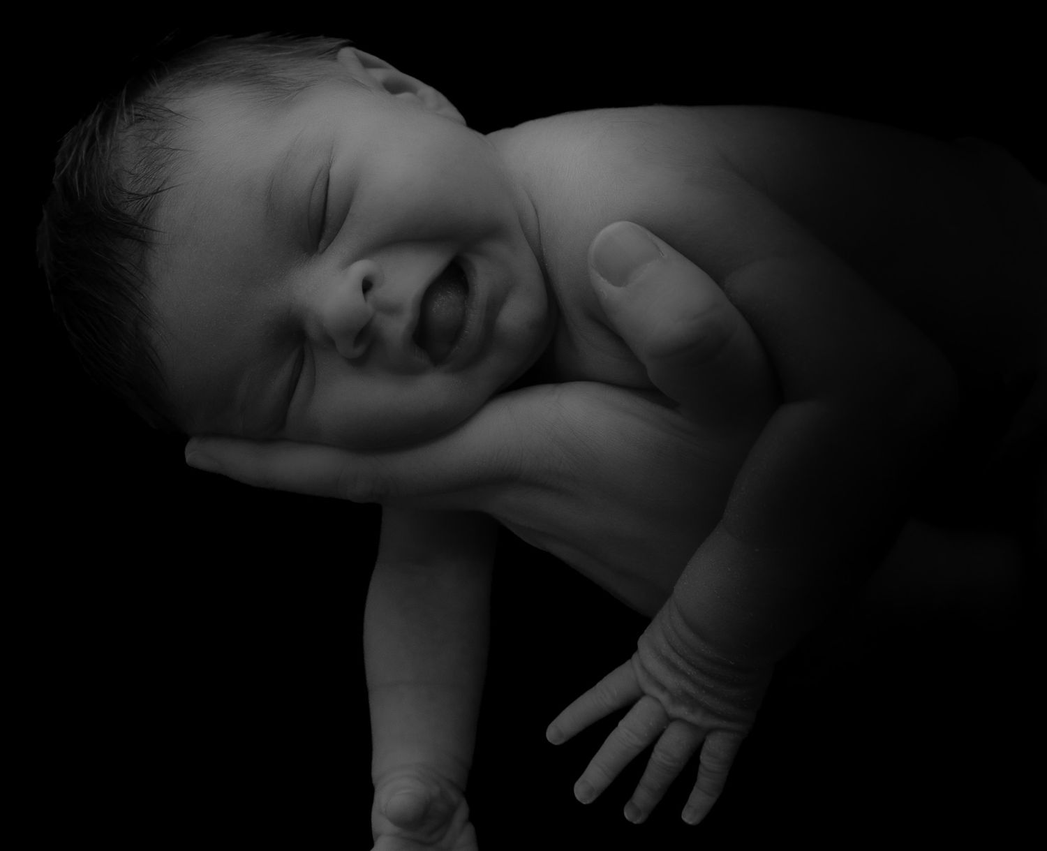 baby photographed resting on their dad's arm with a black background.