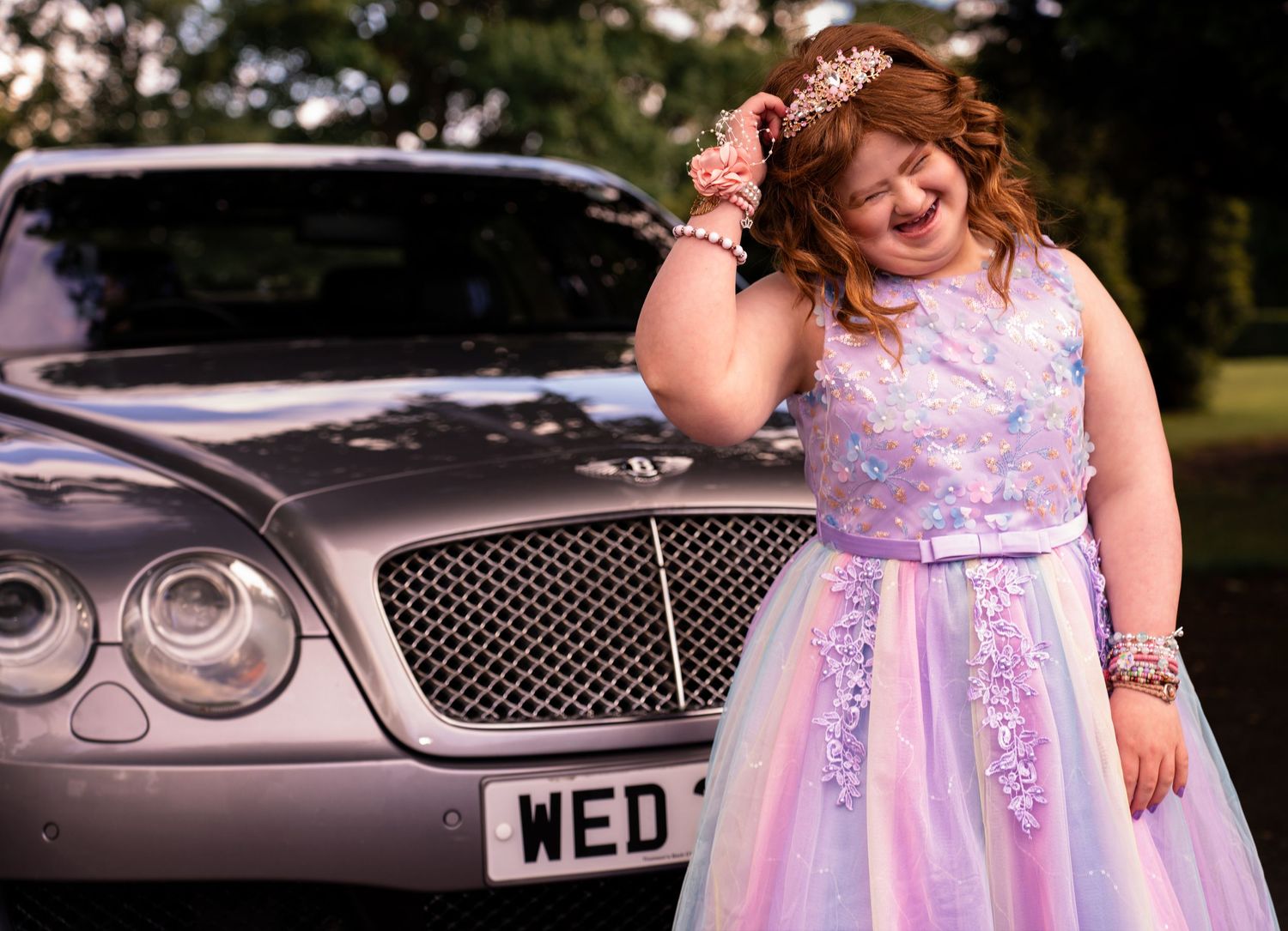 Falkirk prom photography of a young girl in a pink and purple dress with crown posing beside a Bentley from Three Kings Wedding Cars