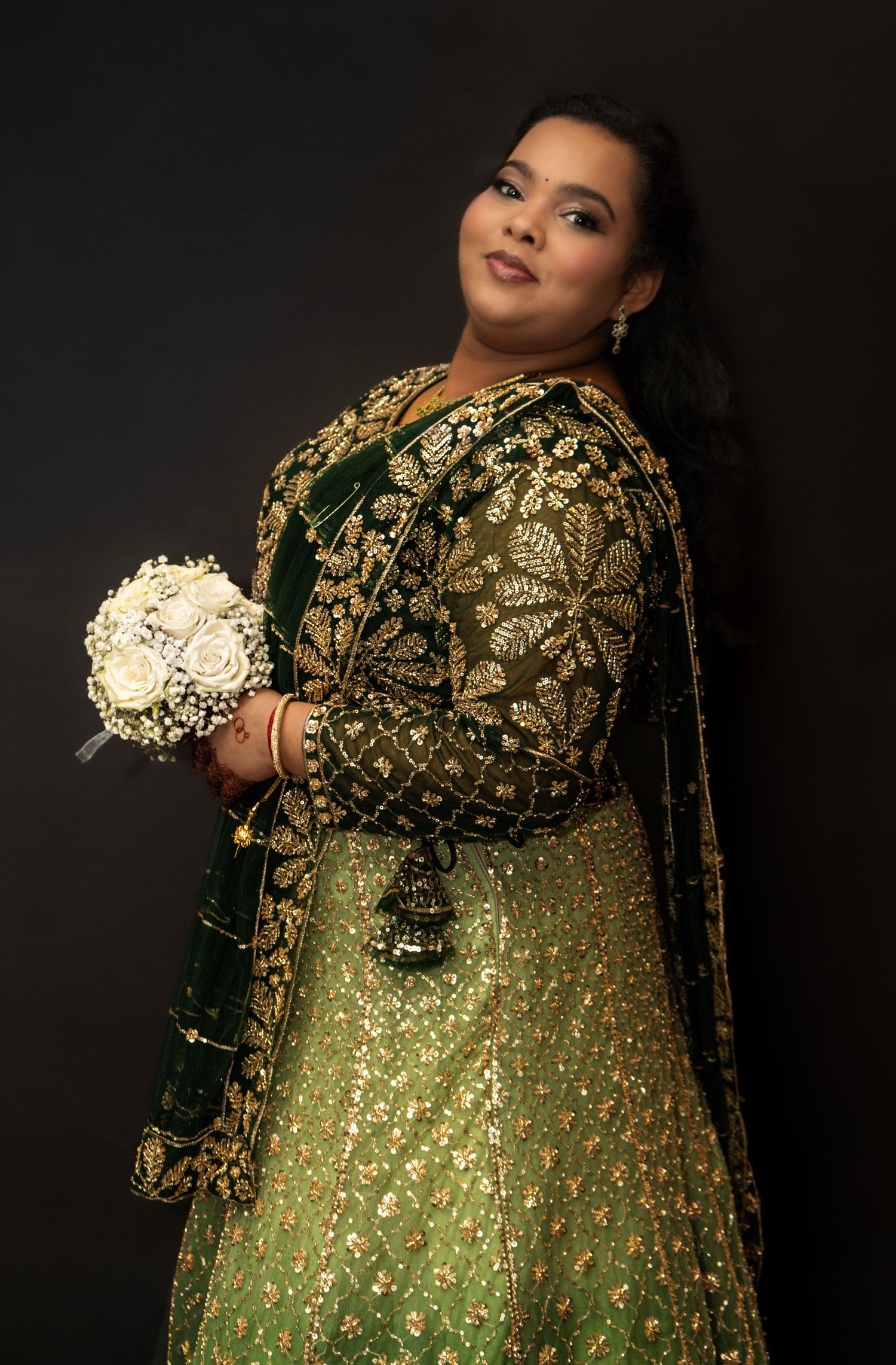 Beautiful Sri Lankan bride in green and gold traditional dress, posing with her bouquet of flowers.