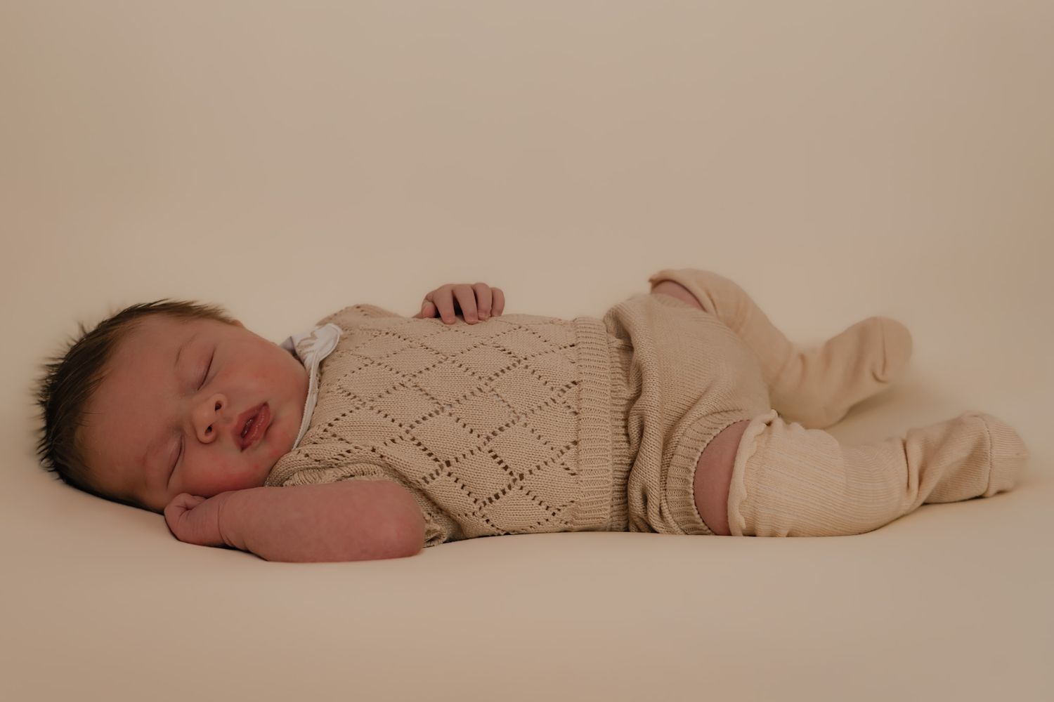 posed newborn photograph of baby boy in nude jampants and long socks.