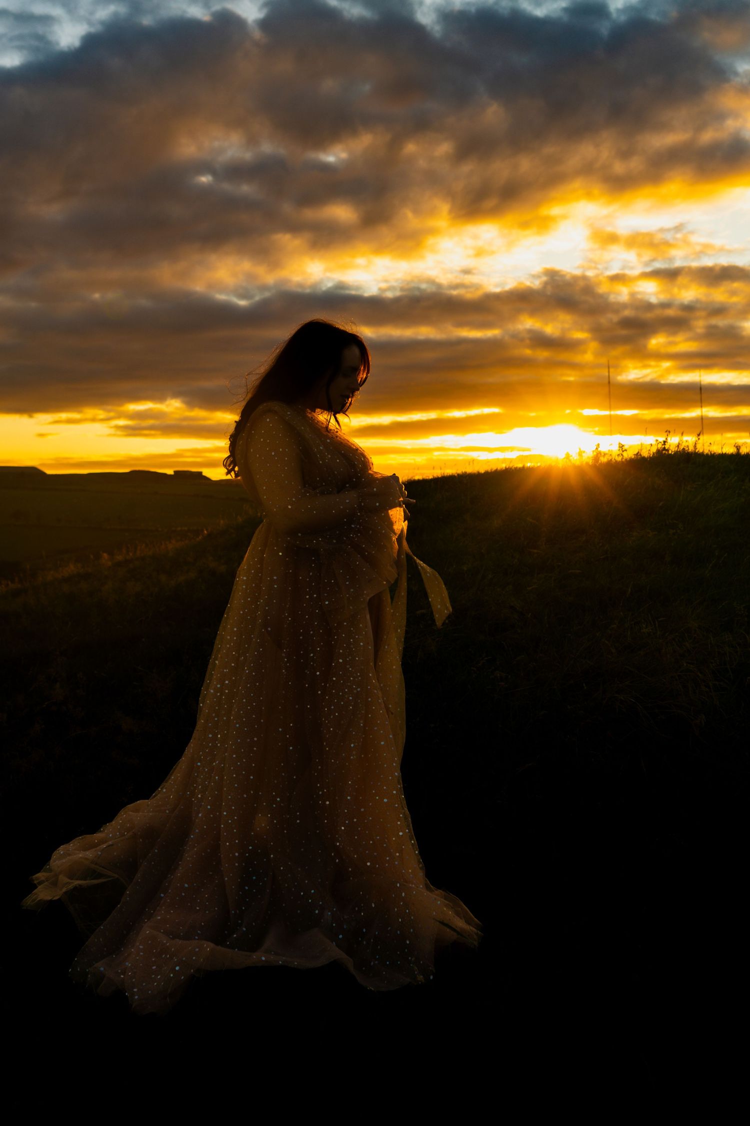 Outdoor maternity photo near Shotts, mum-to-be photographed at sunset looking down at bump.