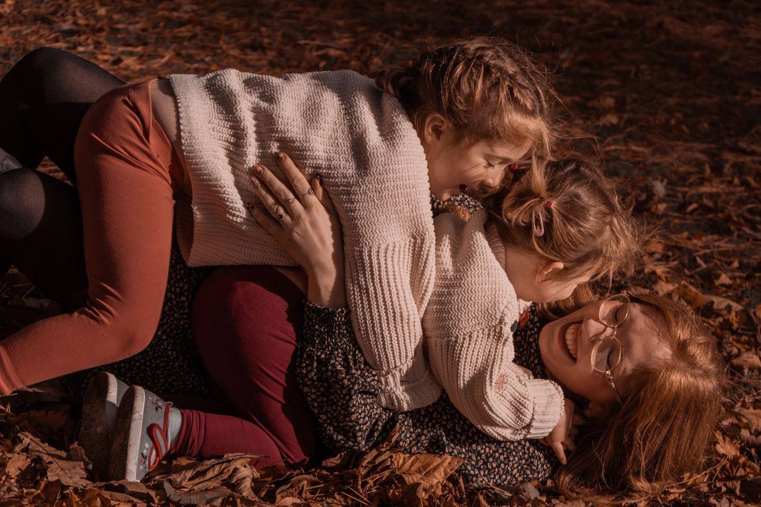 mum and two daughters laughing amongst the leaves at Pittencrief Park in Dunfermline.