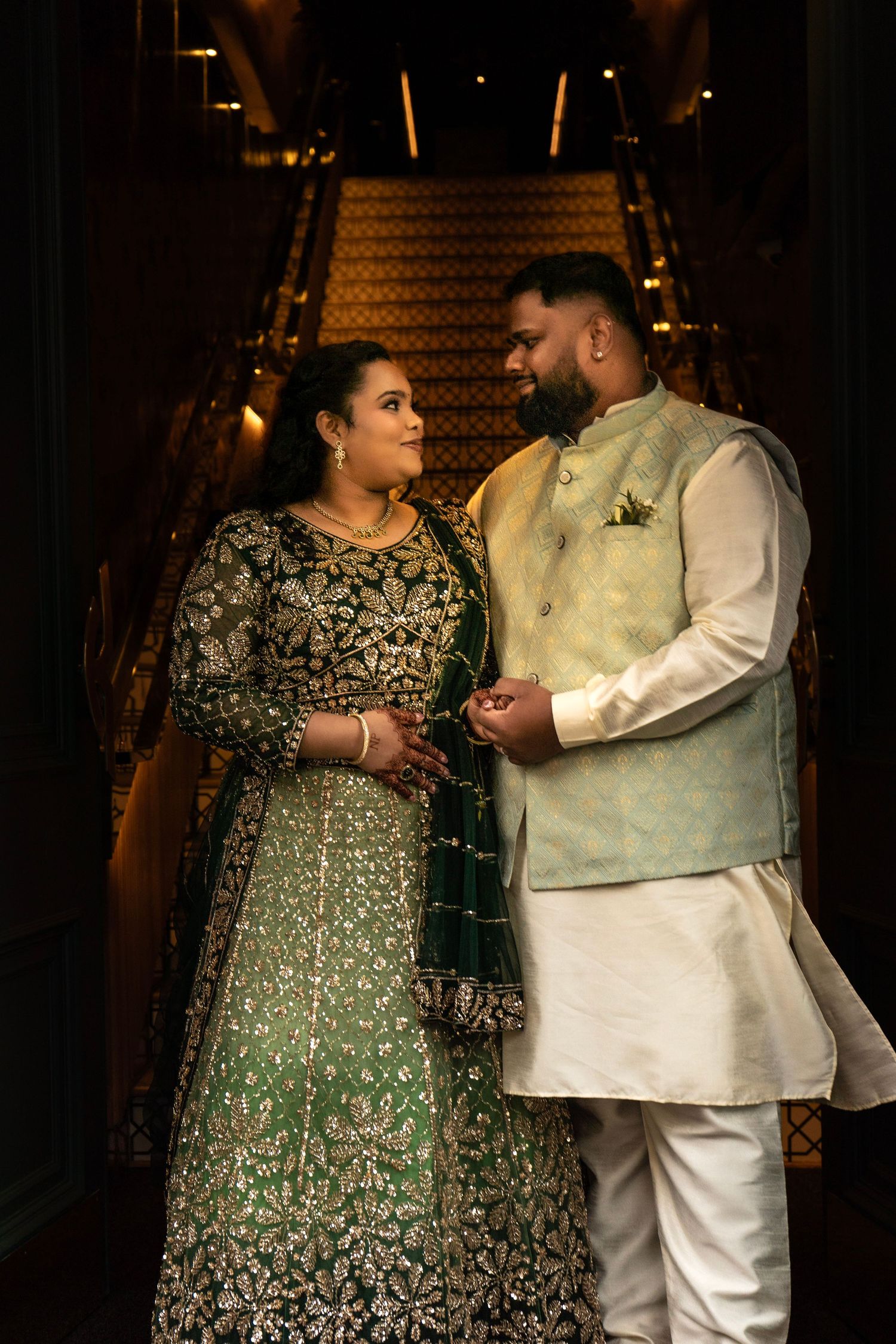 Sri Lankan bride and groom in traditional formal attire, standing together on a dark staircase in a candid portrait moment