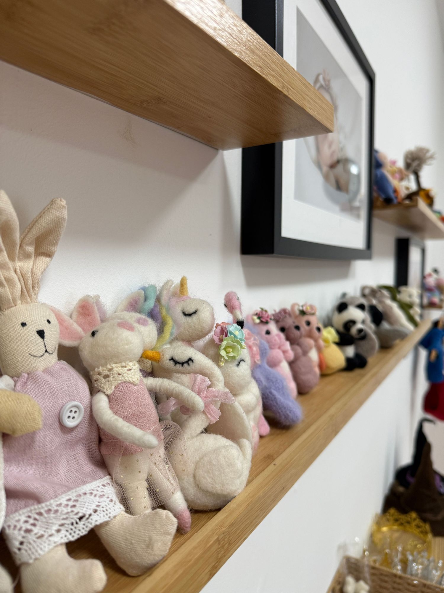 A wooden shelf displays a charming collection of plush stuffed animals including bunnies and a unicorn.