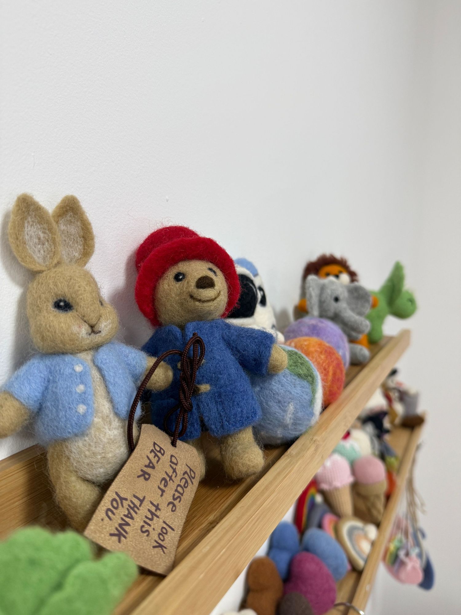 Needle felted Peter Rabbit and Paddington Bear figurines displayed on a wooden shelf with colorful toys.