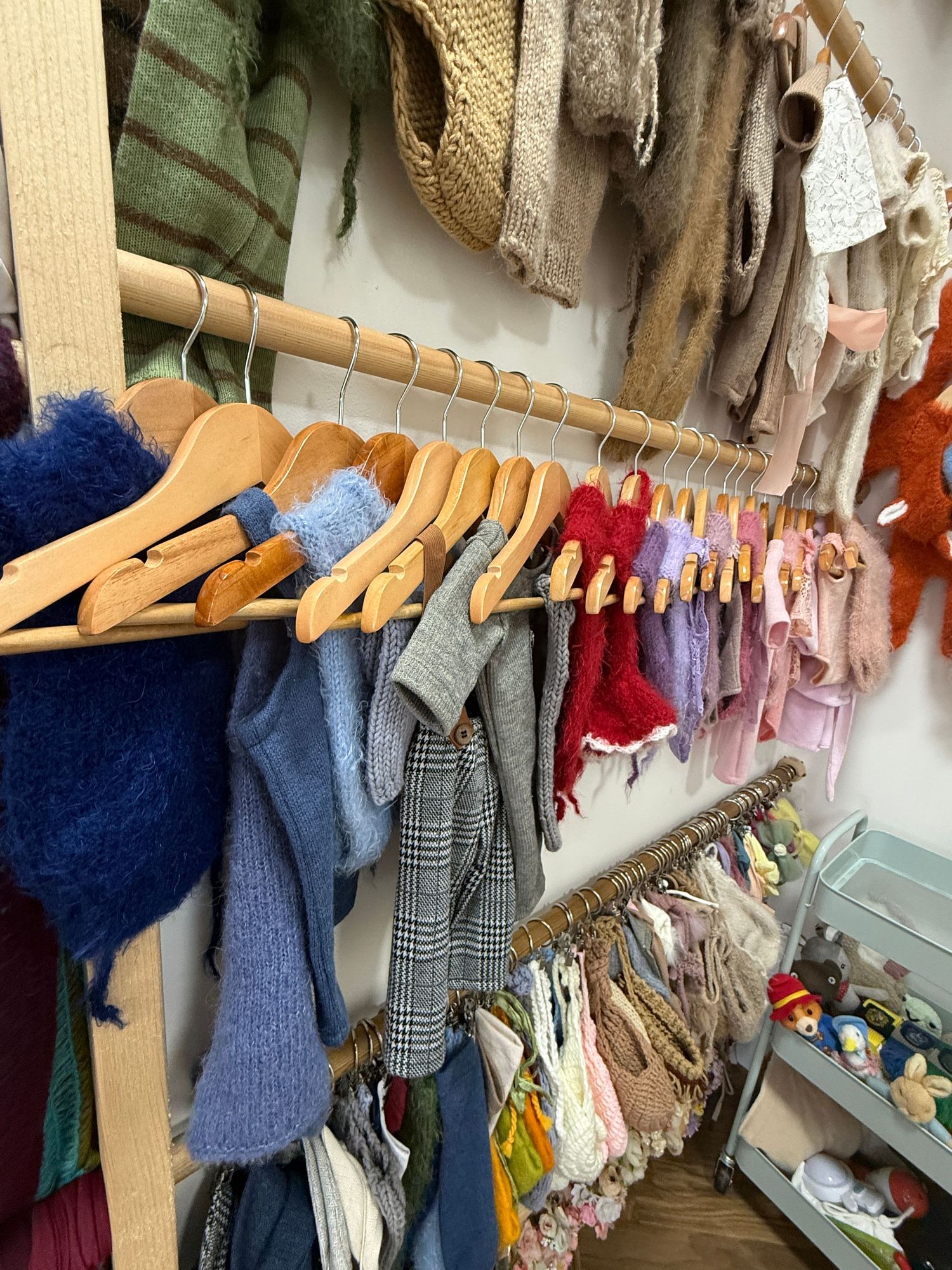 Colorful knit sweaters and scarves displayed on wooden hangers in a boutique clothing store.