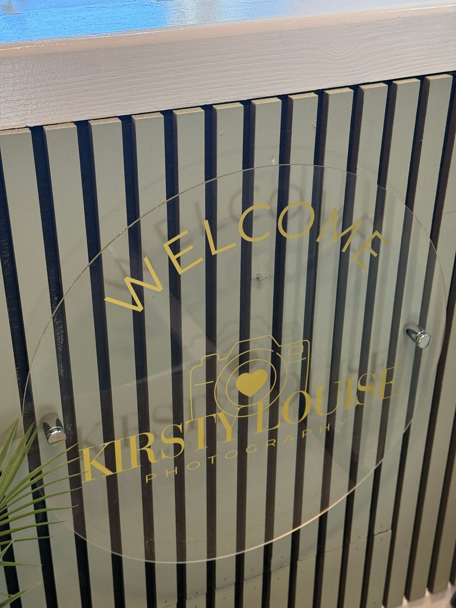 Welcome sign for Kirsty Louise Photography studio displayed on a striped glass door panel.