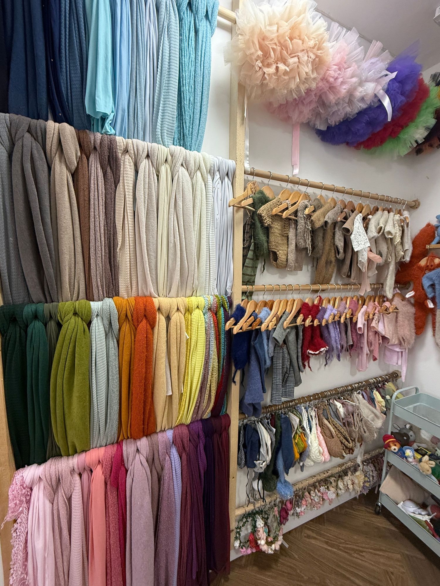 Colorful fabric rolls and children's clothing displayed on wooden racks in a boutique shop.
