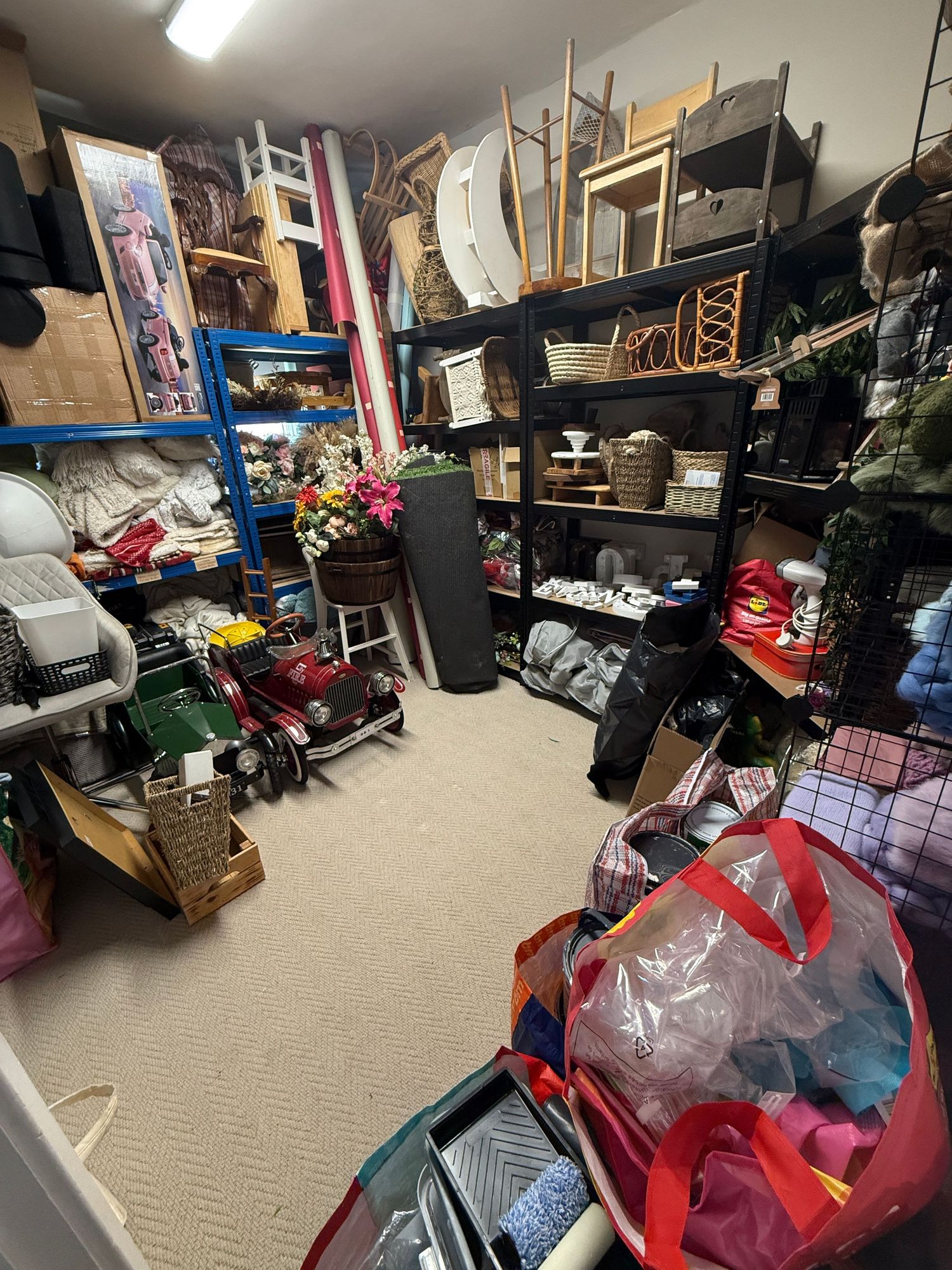 Cluttered storage room with shelves filled with misc items, baskets, flowers, bags, and various household goods.