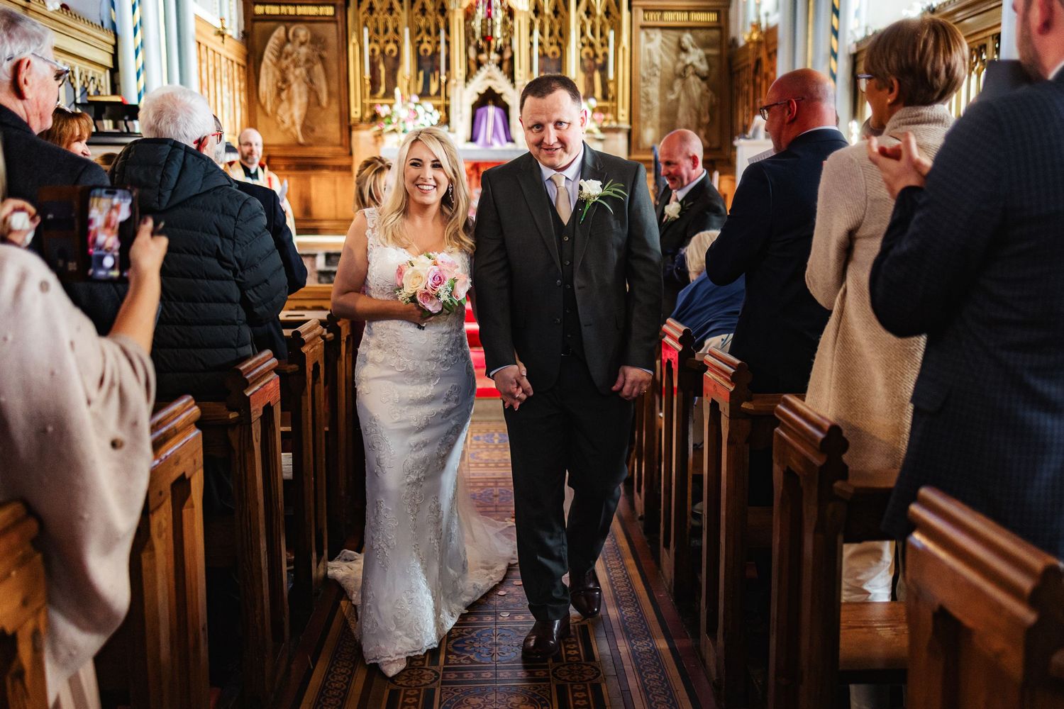Bride and groom walking down church aisle after wedding ceremony, smiling with guests seated in pews.