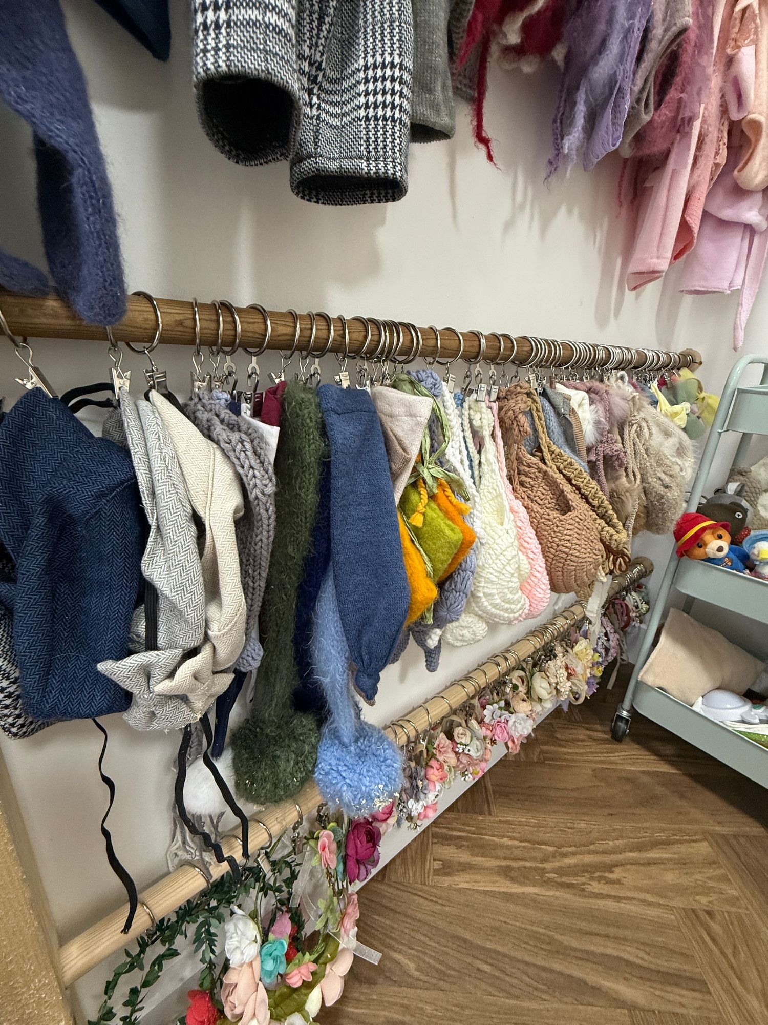 A clothing rack with sweaters, bags, and garments displayed in a boutique shop with floral decorations below.