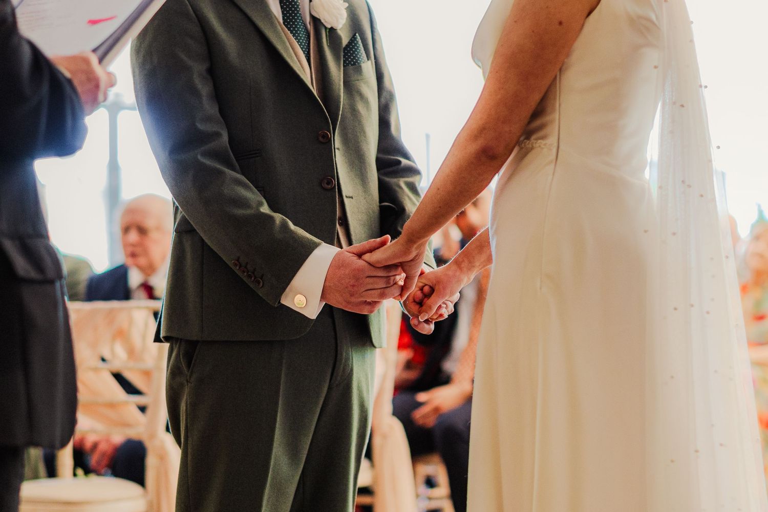 Bride and groom holding hands during wedding ceremony, exchanging rings at the altar in elegant attire.