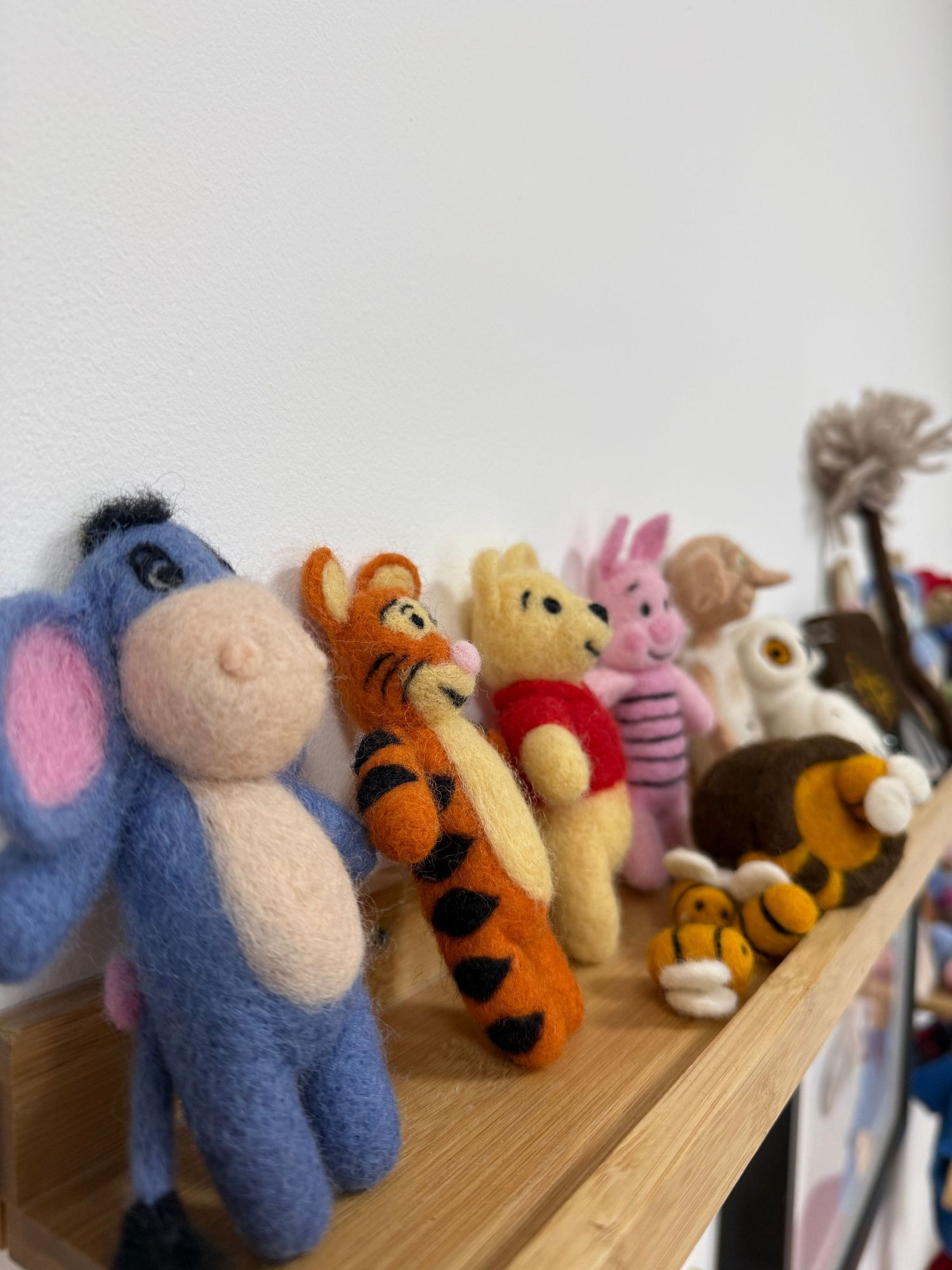 Needle felted Winnie the Pooh characters including Eeyore, Tigger, Pooh, and Piglet displayed on a wooden shelf.