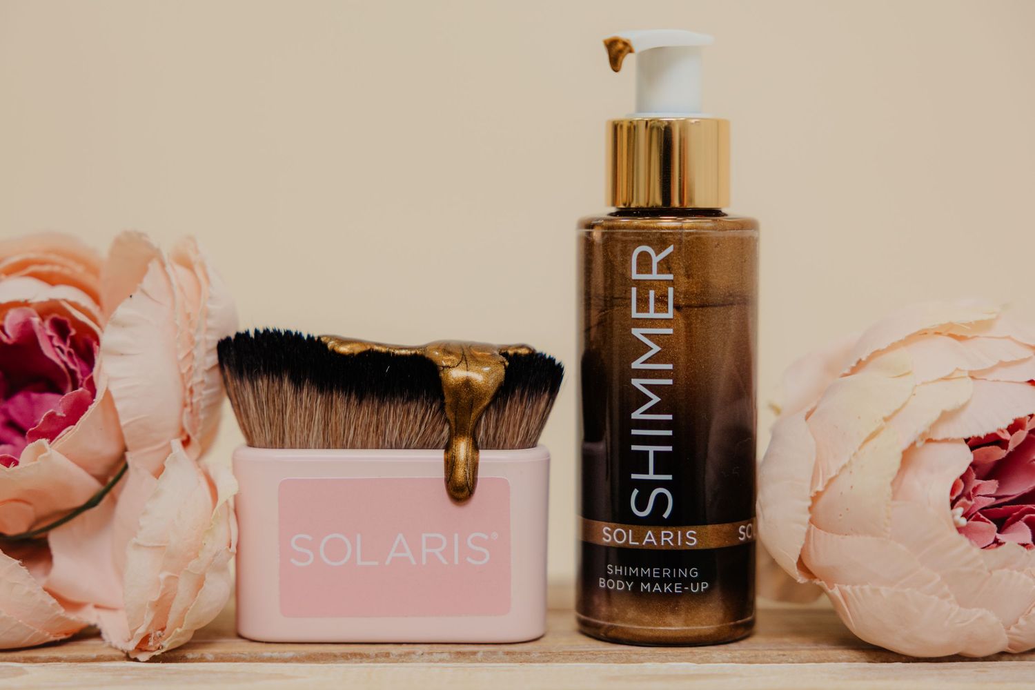 Solaris Shimmer bronzing body makeup bottle and pink brush holder surrounded by pink peonies on a beige background.Kirsty Louise Photography