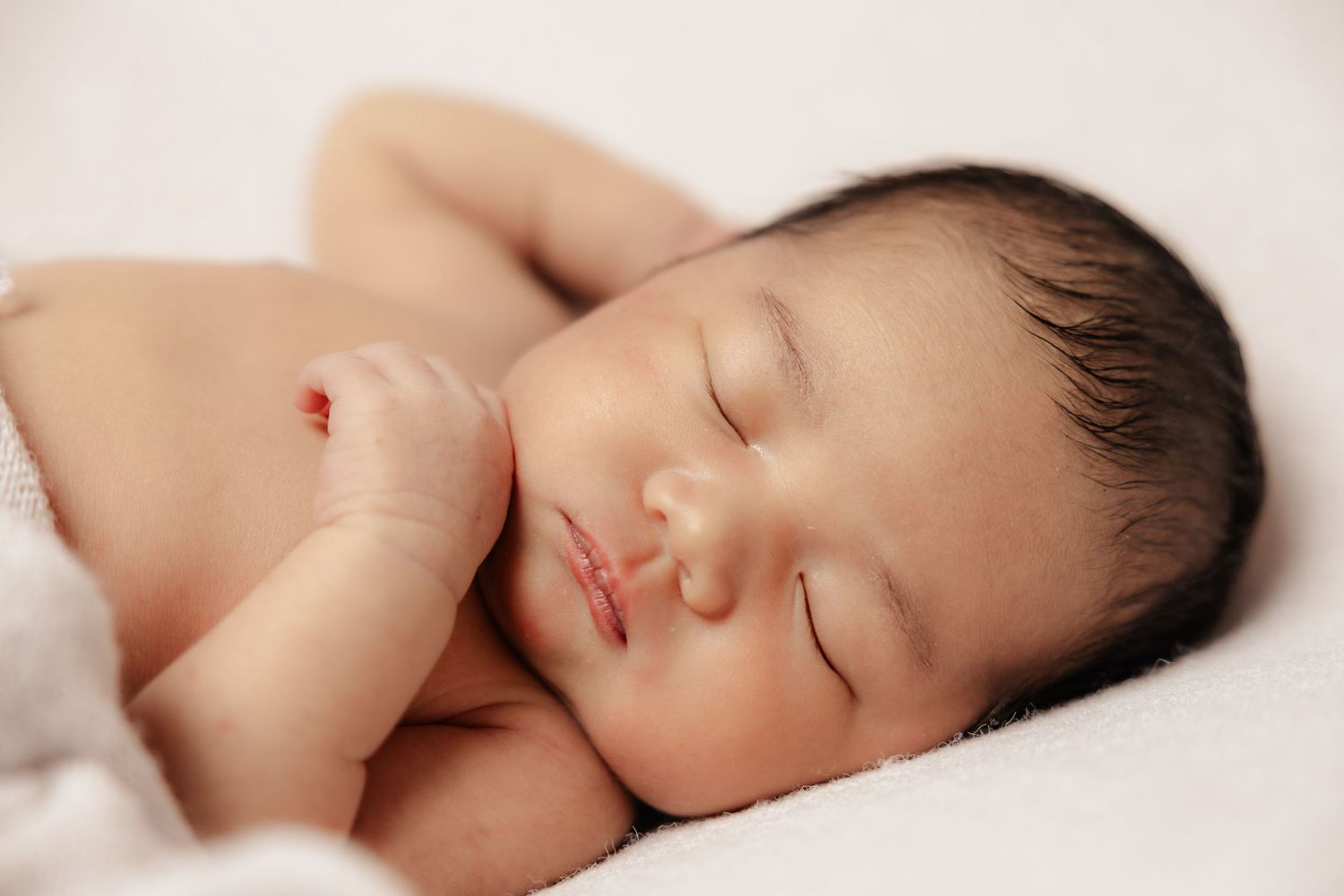 Peaceful sleeping newborn wrapped in soft white fabric against cream background.photographer wigan