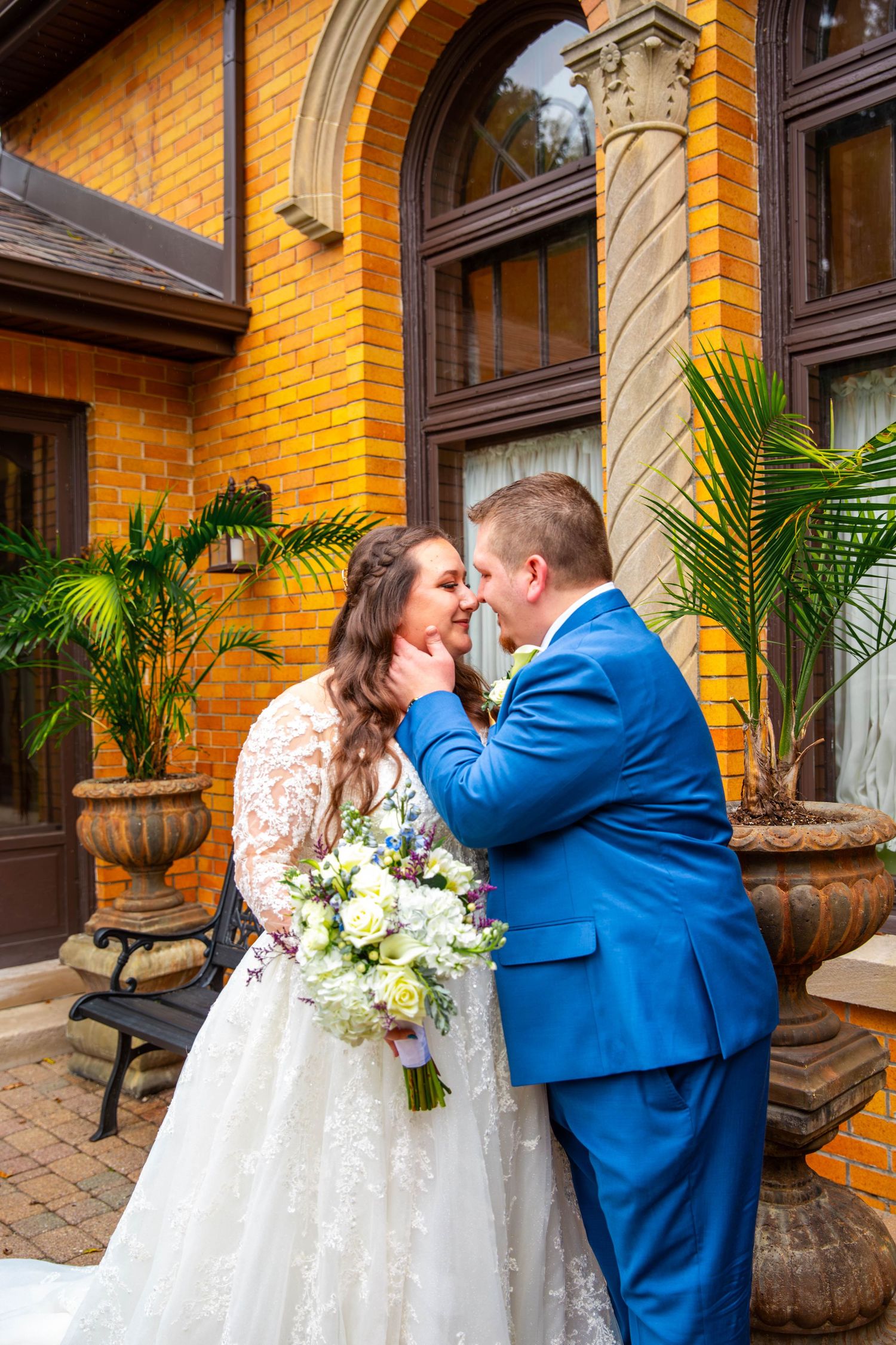 Wedding couple sharing a moment on a yellow brick building's porch with tropical plants.