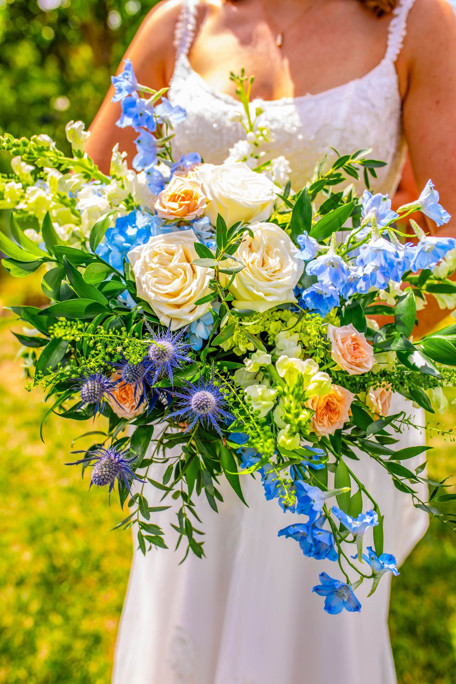 Beautiful bridal bouquet featuring blue delphiniums, white roses, and peach accents.