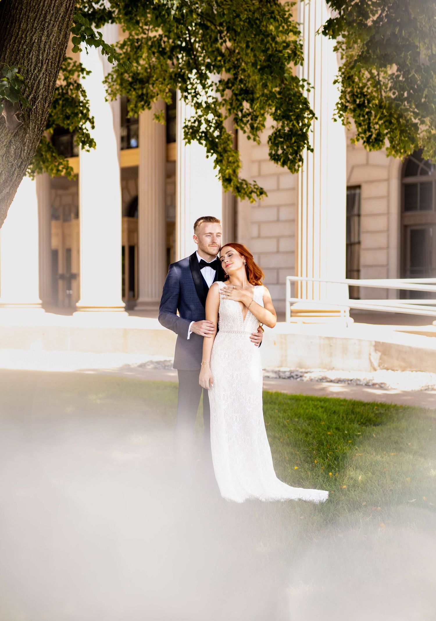 Elegant wedding portrait taken in front of a classical stone building with columns.