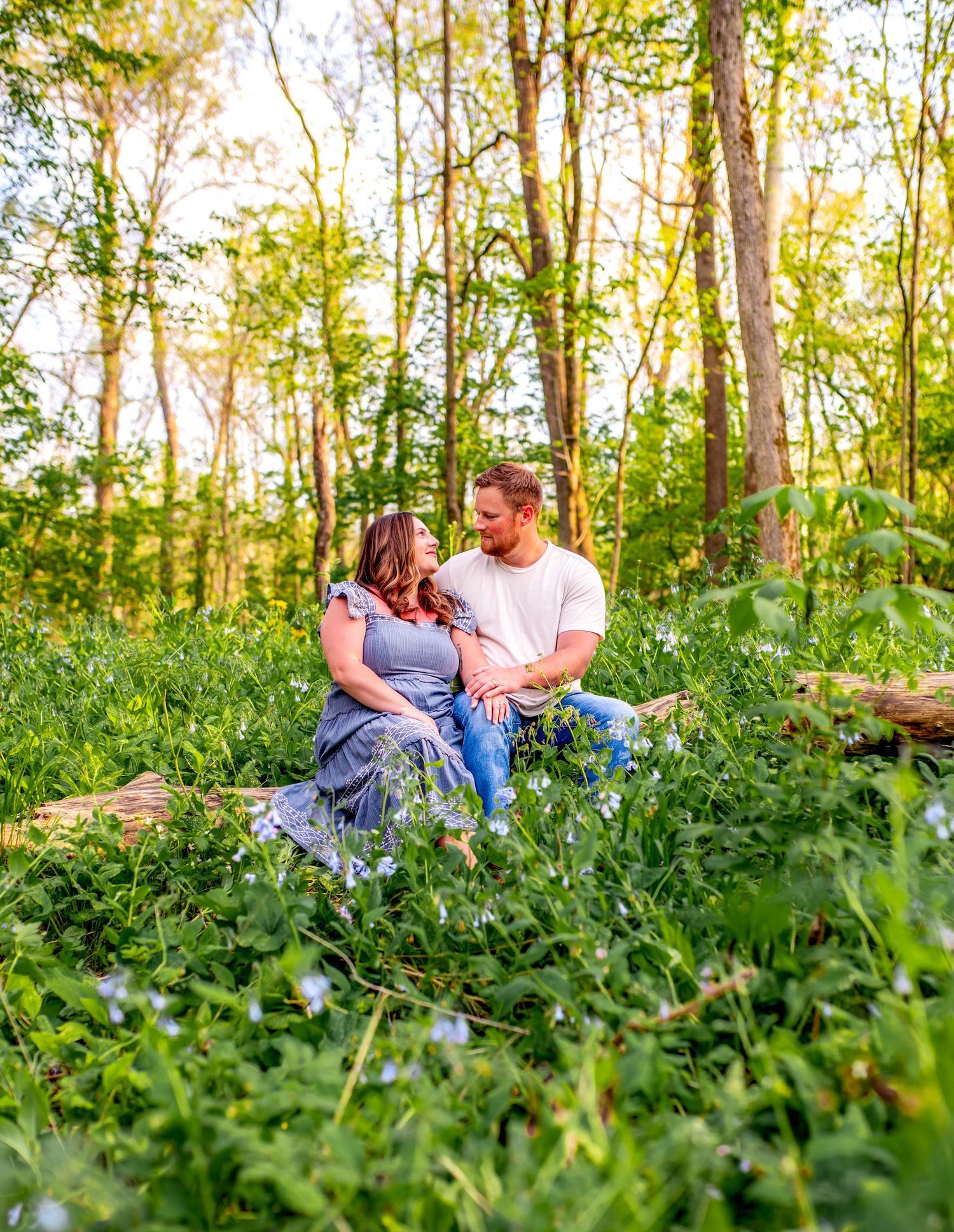 Couple sits together in a lush green forest clearing during sunset.