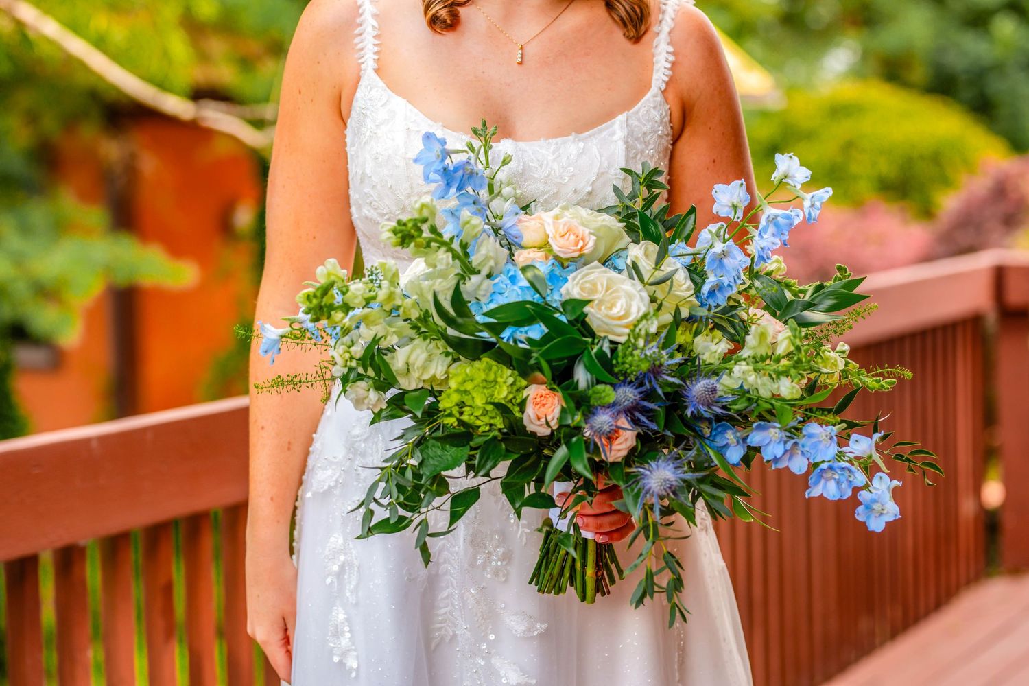 Elegant bridal bouquet with blue and white flowers against natural outdoor background.