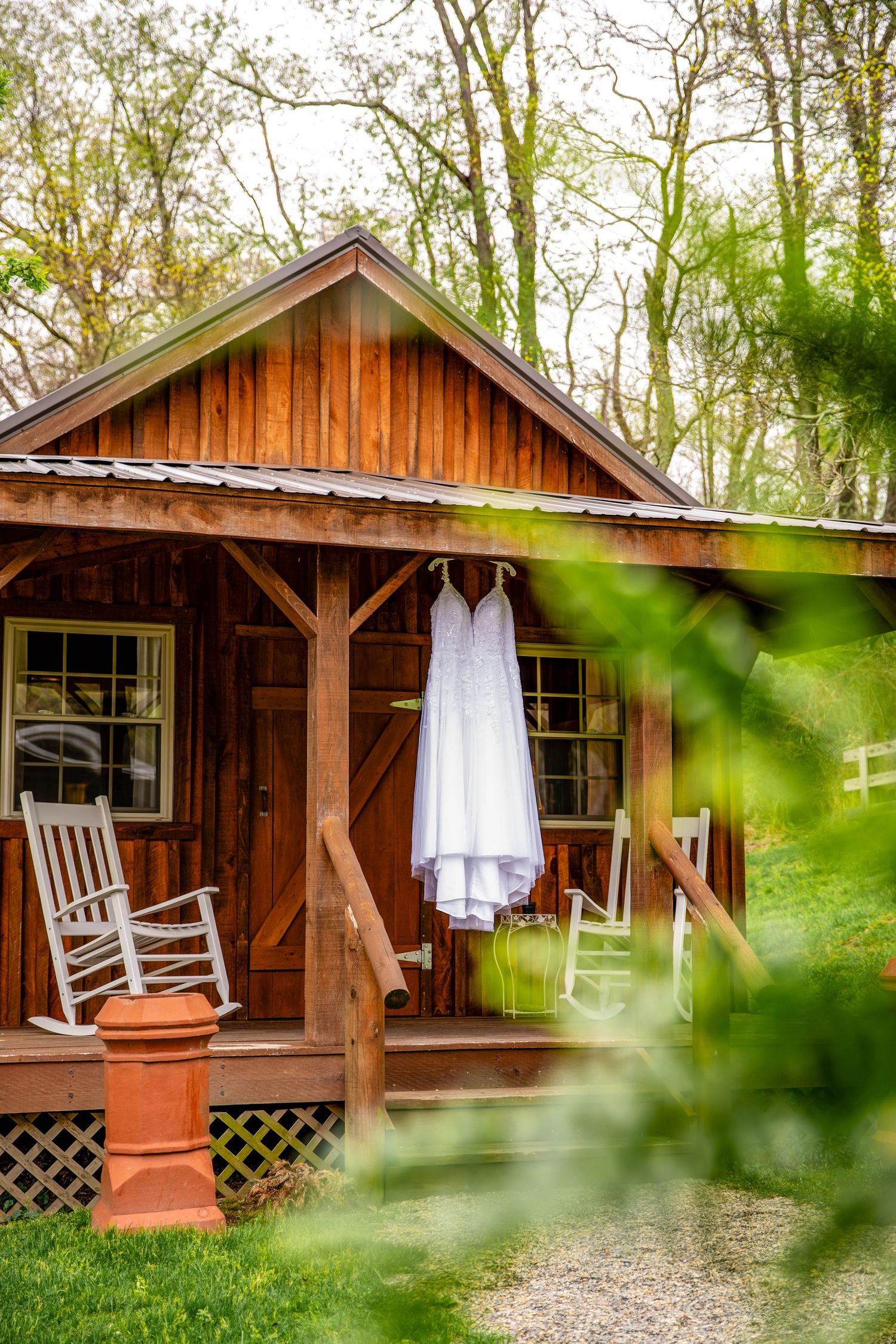 Rustic wooden cabin with white rocking chairs and porch details captured through green foliage.