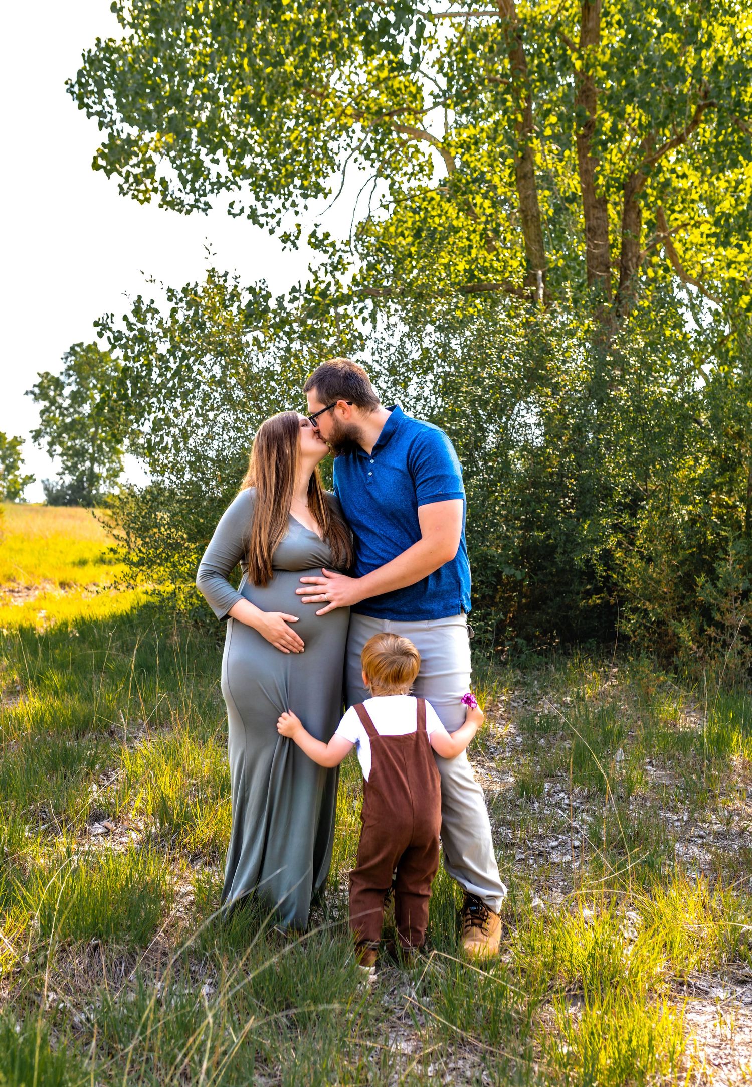 Family maternity photoshoot in a natural outdoor setting with golden sunlight.