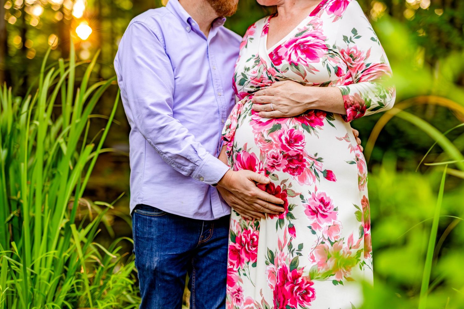 Intimate maternity photo session in garden with floral dress and purple shirt.