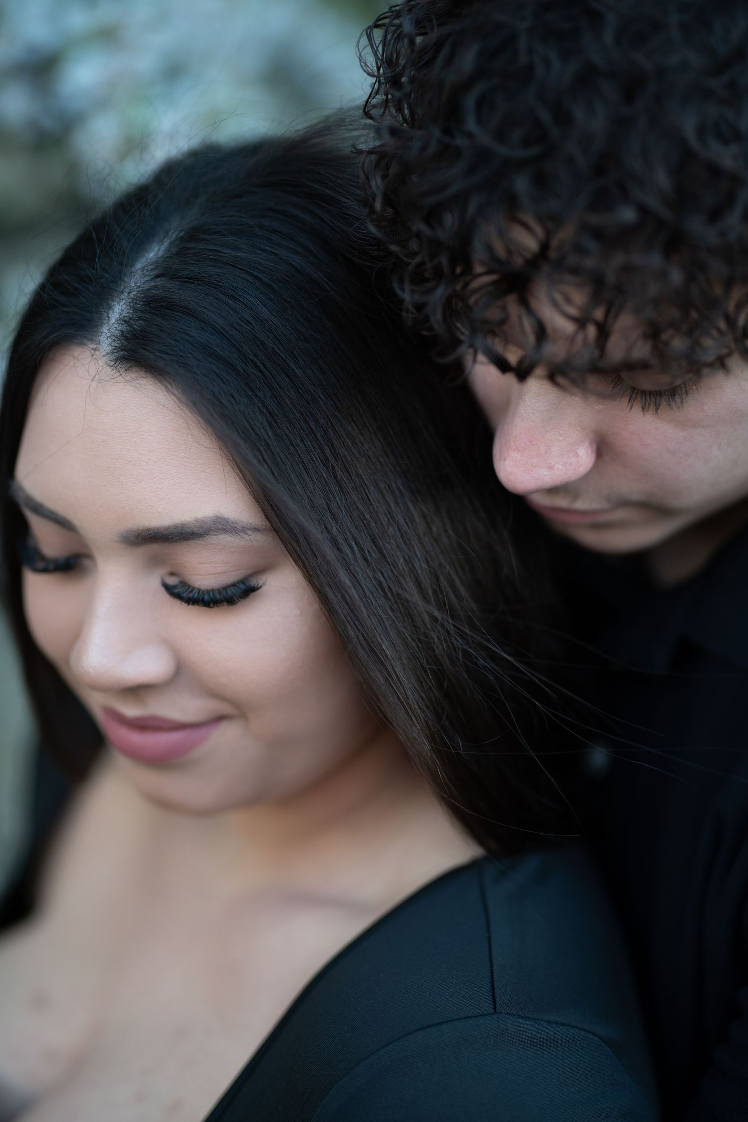 A romantic couple shares an intimate moment with soft lighting and dark curly hair against a blurred background.