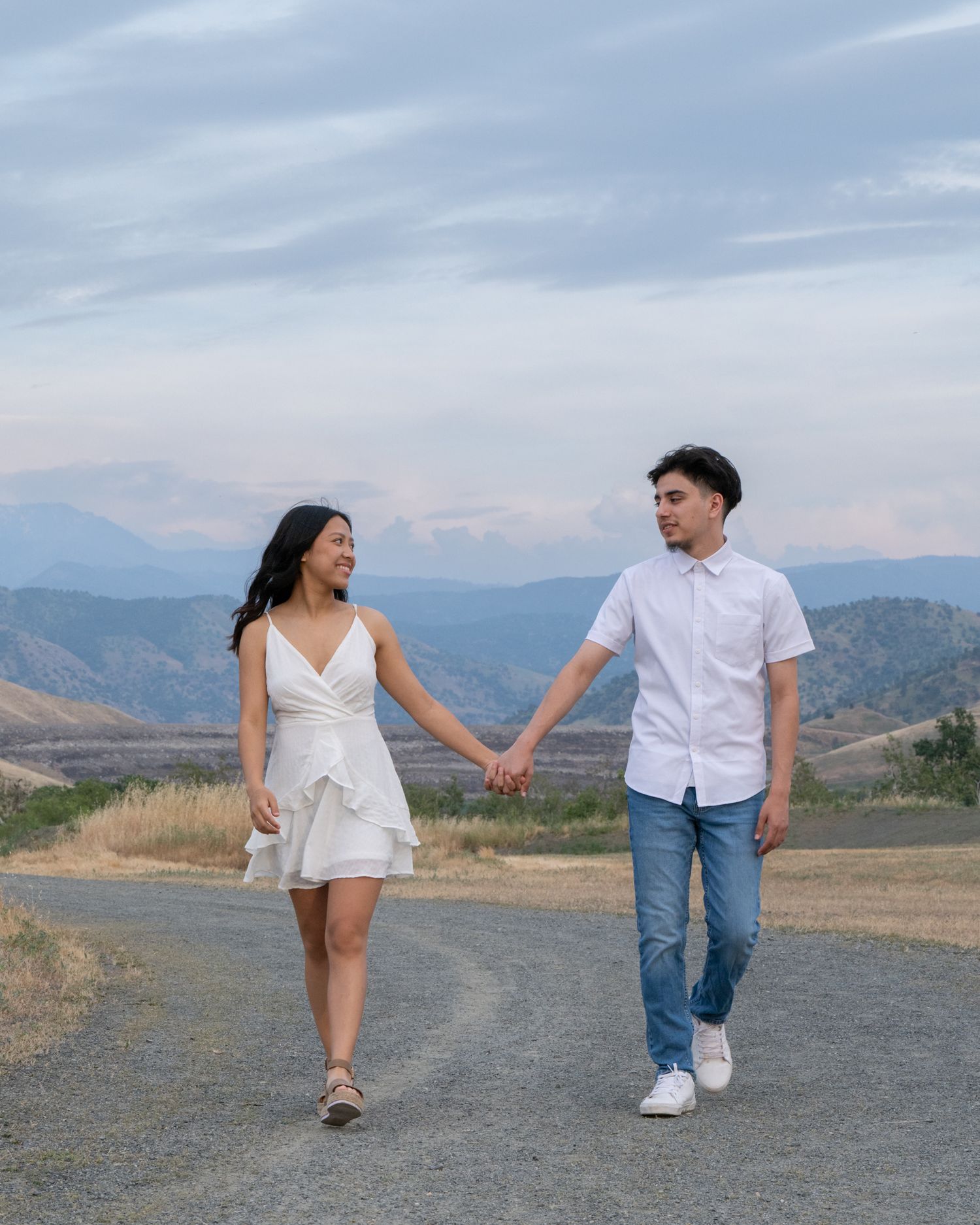 Couple walking hand in hand on a mountain path with scenic valley views in the background.