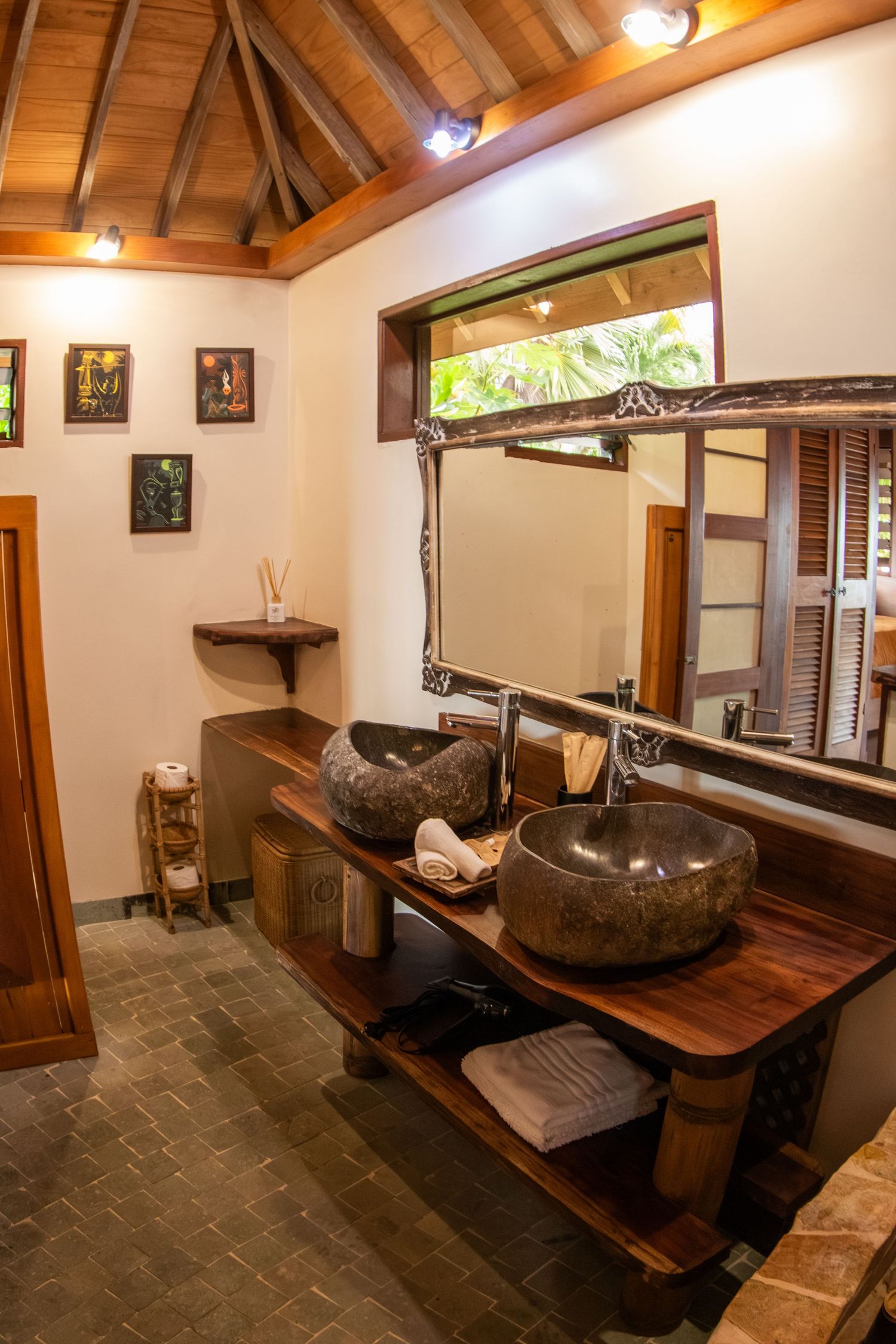 Interior view of a rustic bathroom with wooden beams, stone sink, and natural light streaming through window.