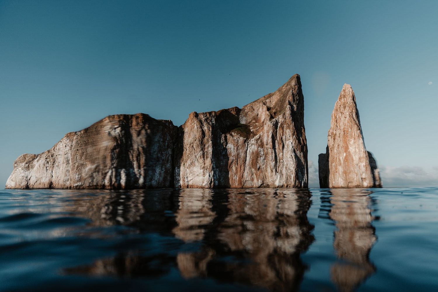 Dramatic rocky cliffs rise from calm ocean waters under a blue sky.