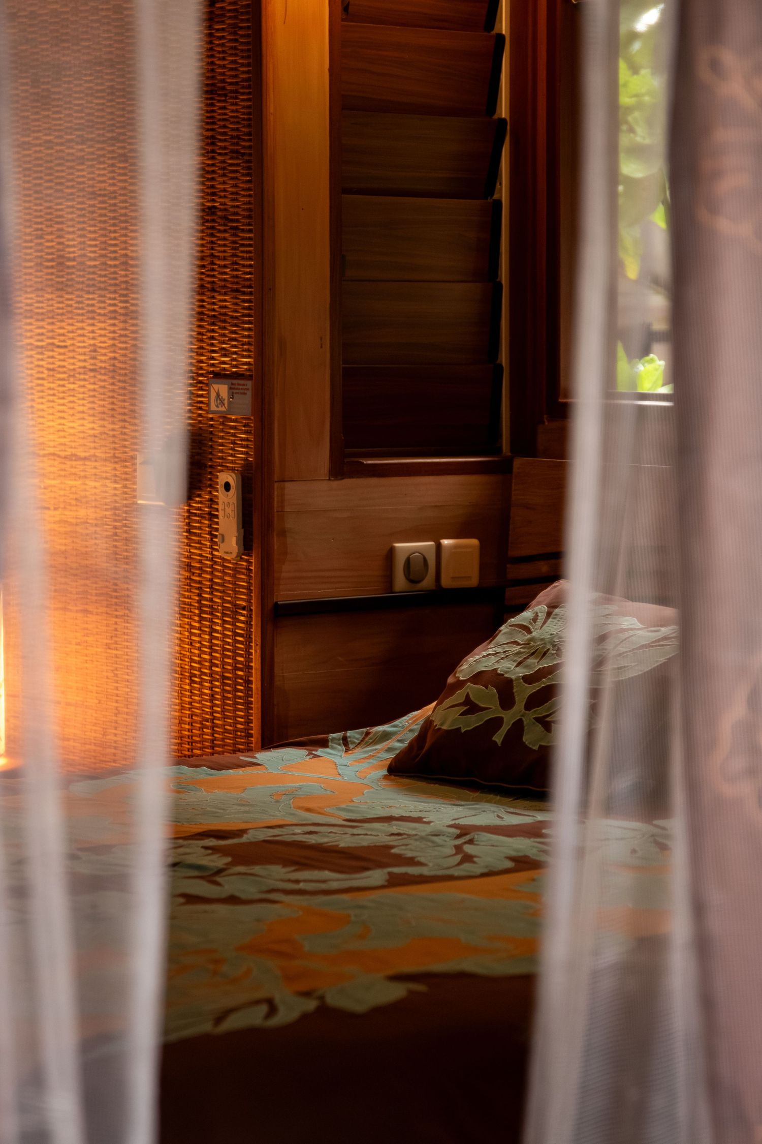 Interior view of a room with bamboo window blinds casting warm orange light and shadows on a textured surface.