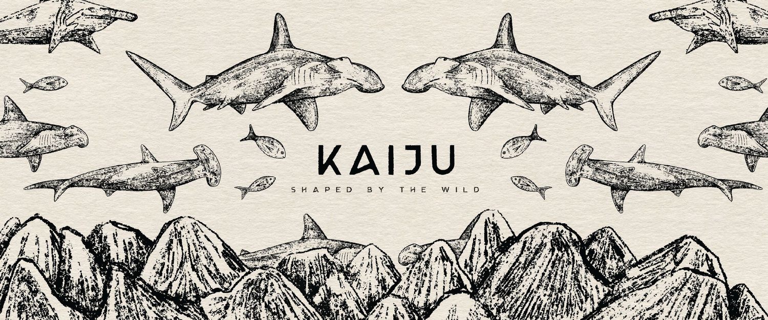 Kaiju brand logo with hand-drawn hammerhead sharks and mountain illustrations, styled with 'Shaped by the Wild' tagline.