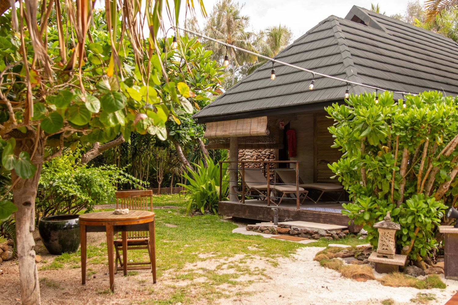 A tropical garden path leads to a wooden gazebo structure surrounded by lush green foliage and palm trees.