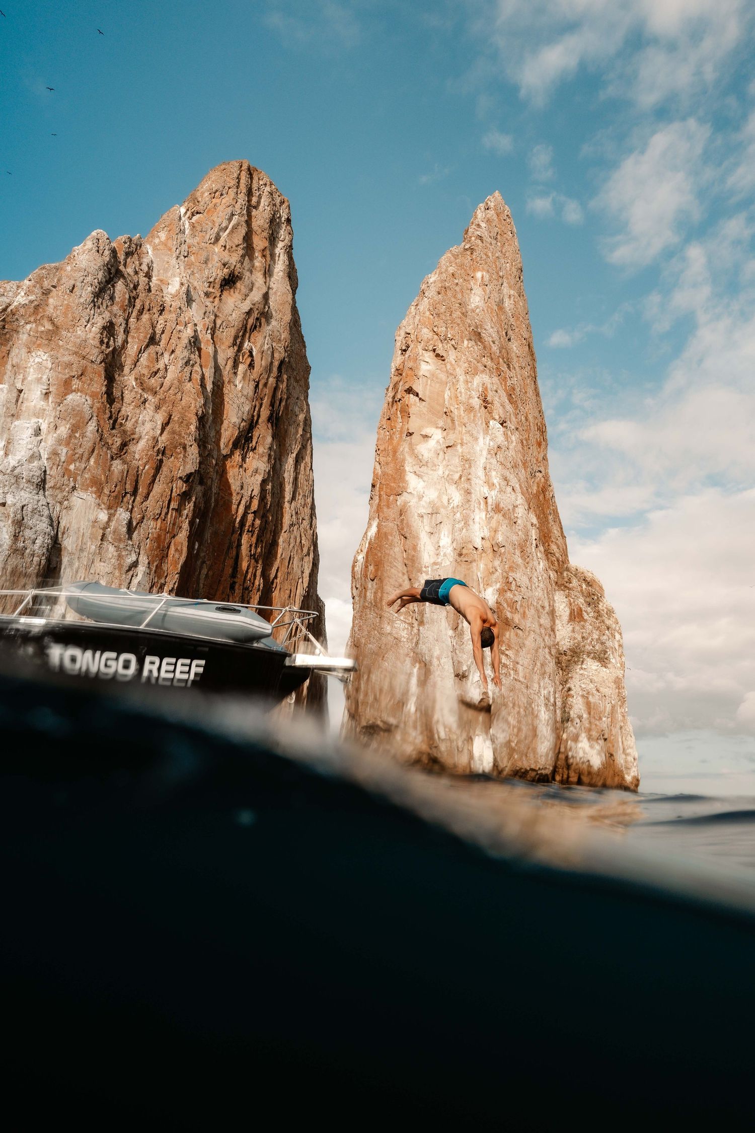 Split underwater view of towering rock formations with boat visible above water surface.