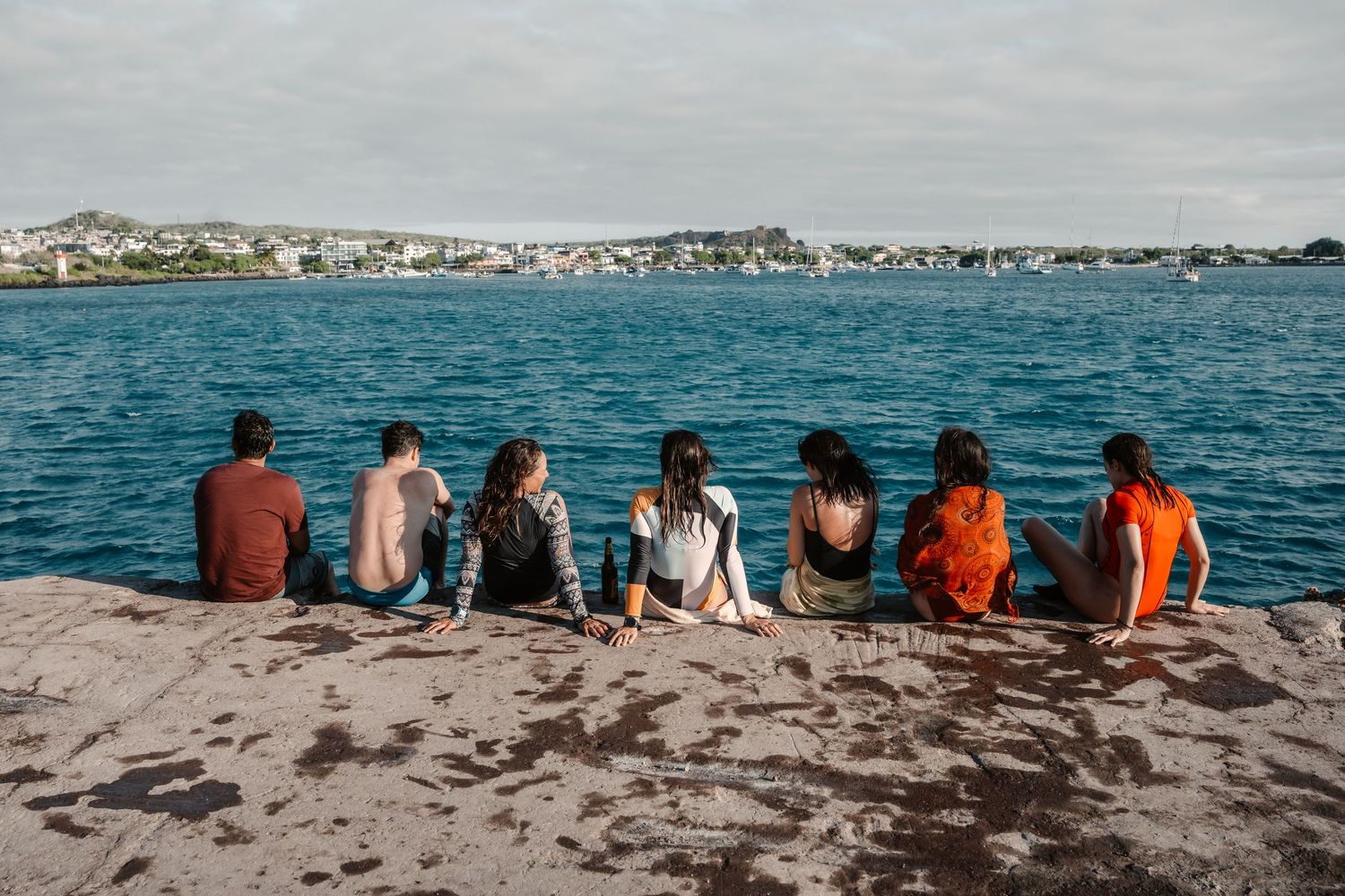Group of visitors sitting on rocky shore overlooking the ocean.
