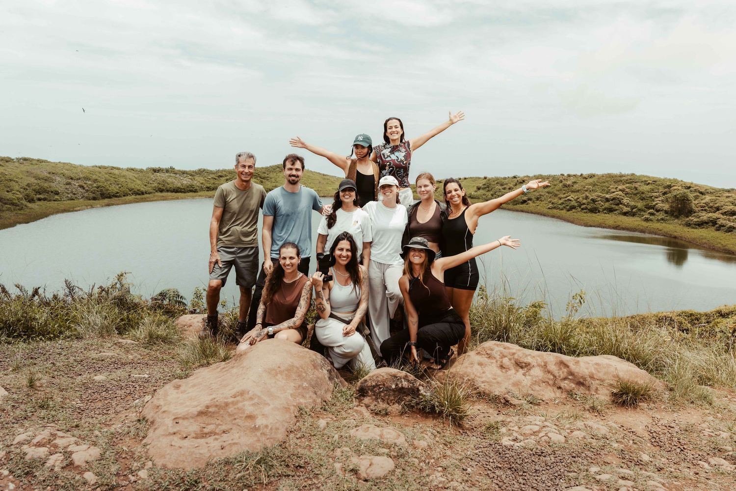 Group of friends sitting together on scenic rocky overlook with lake and mountains in background.