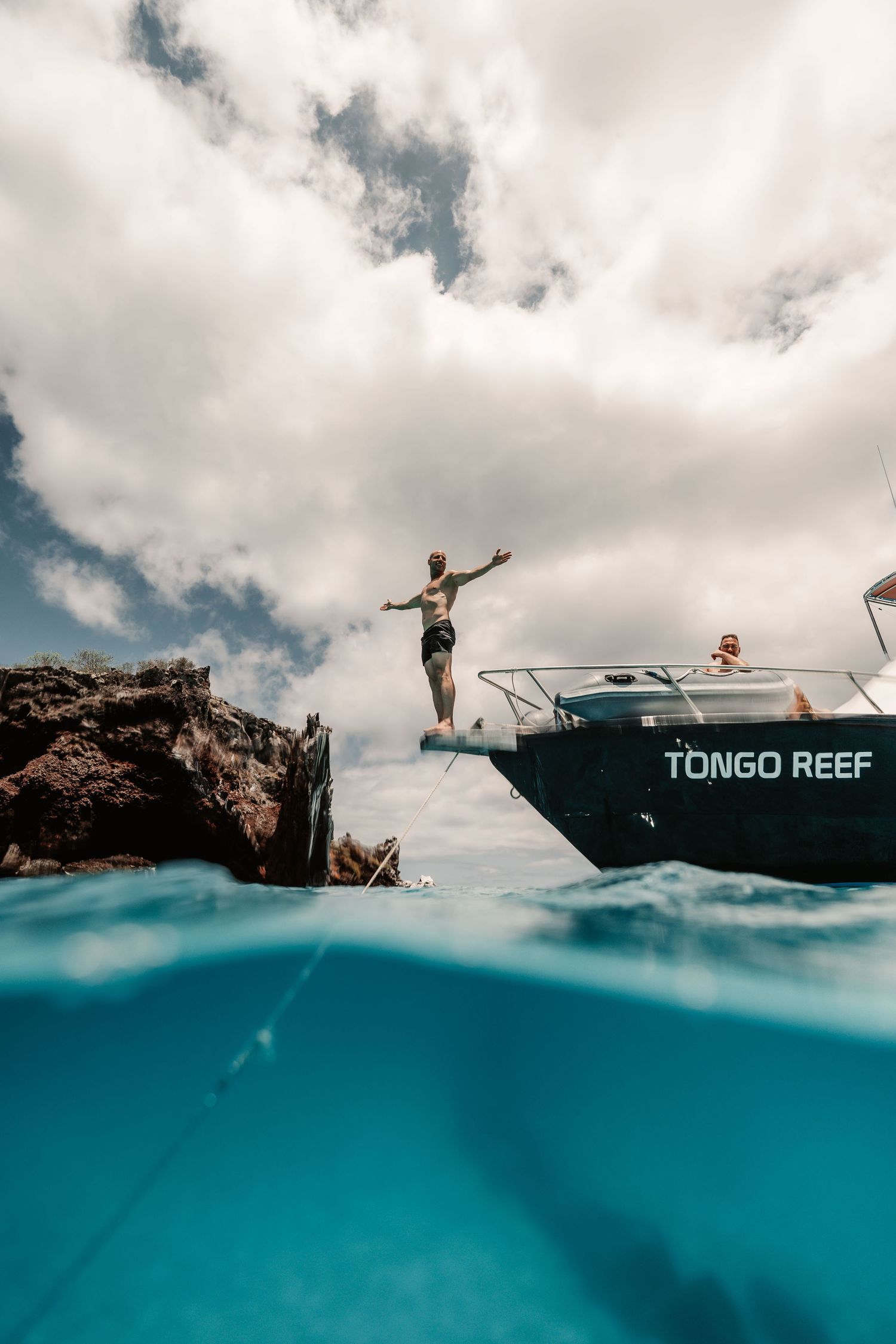 Split-level photo of boat named Tongo Reef with people jumping into clear blue water.