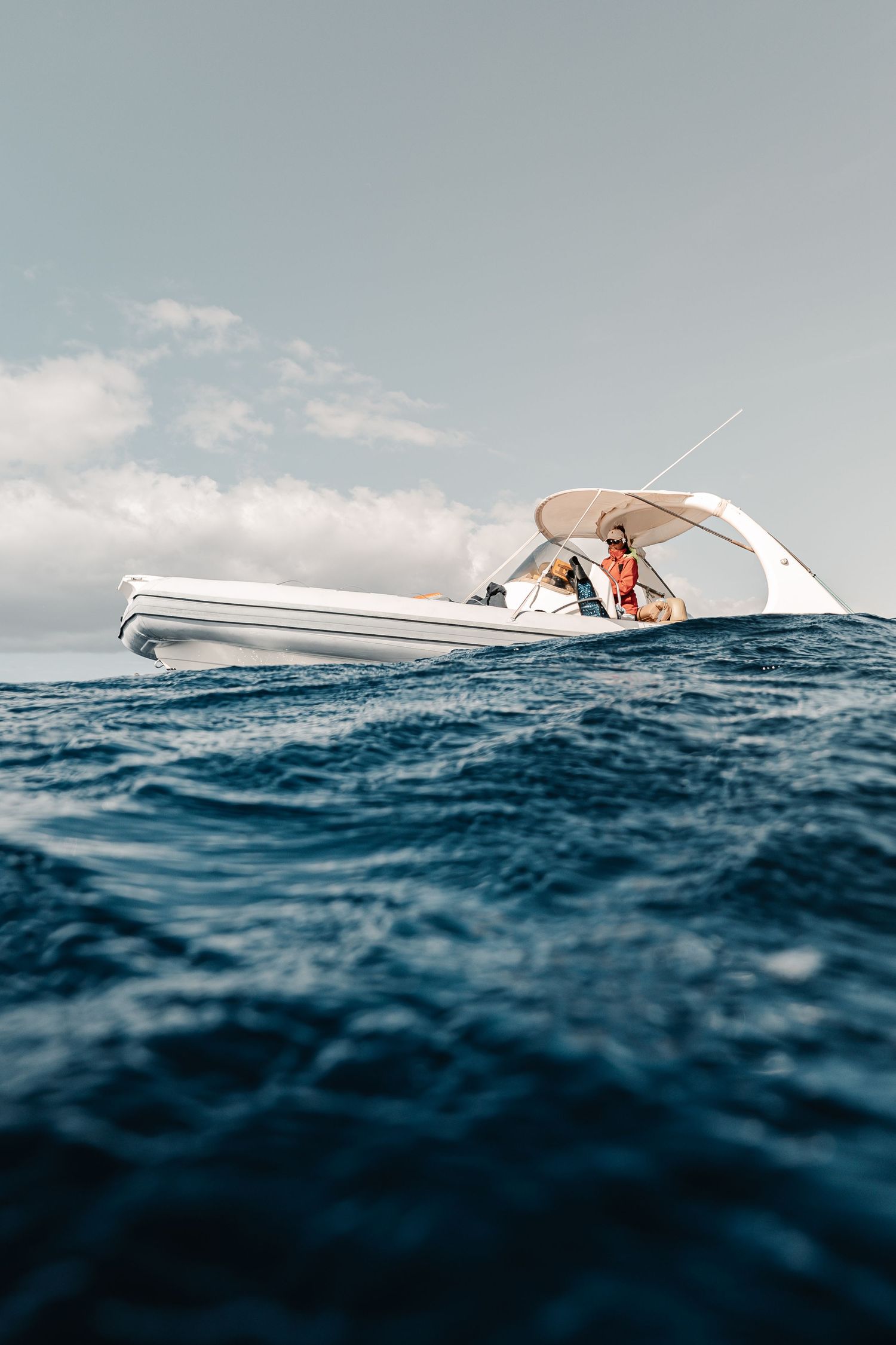A white inflatable RIB speedboat with passengers navigates choppy deep blue ocean waters under a partly cloudy sky.