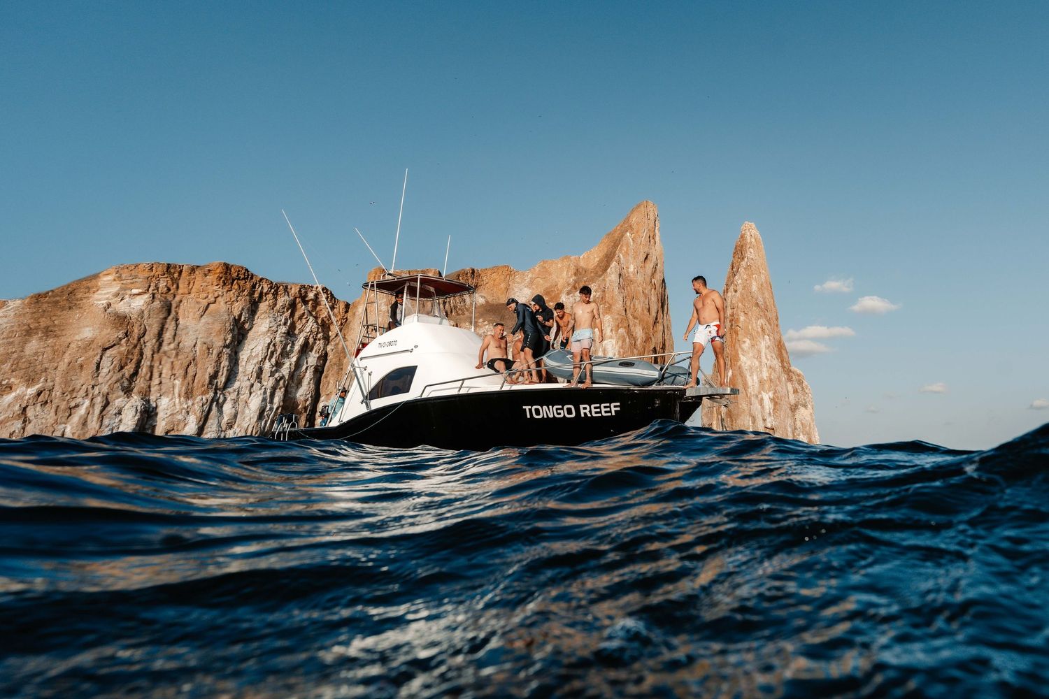 A white yacht cruises past dramatic coastal rock formations rising from deep blue ocean waters.