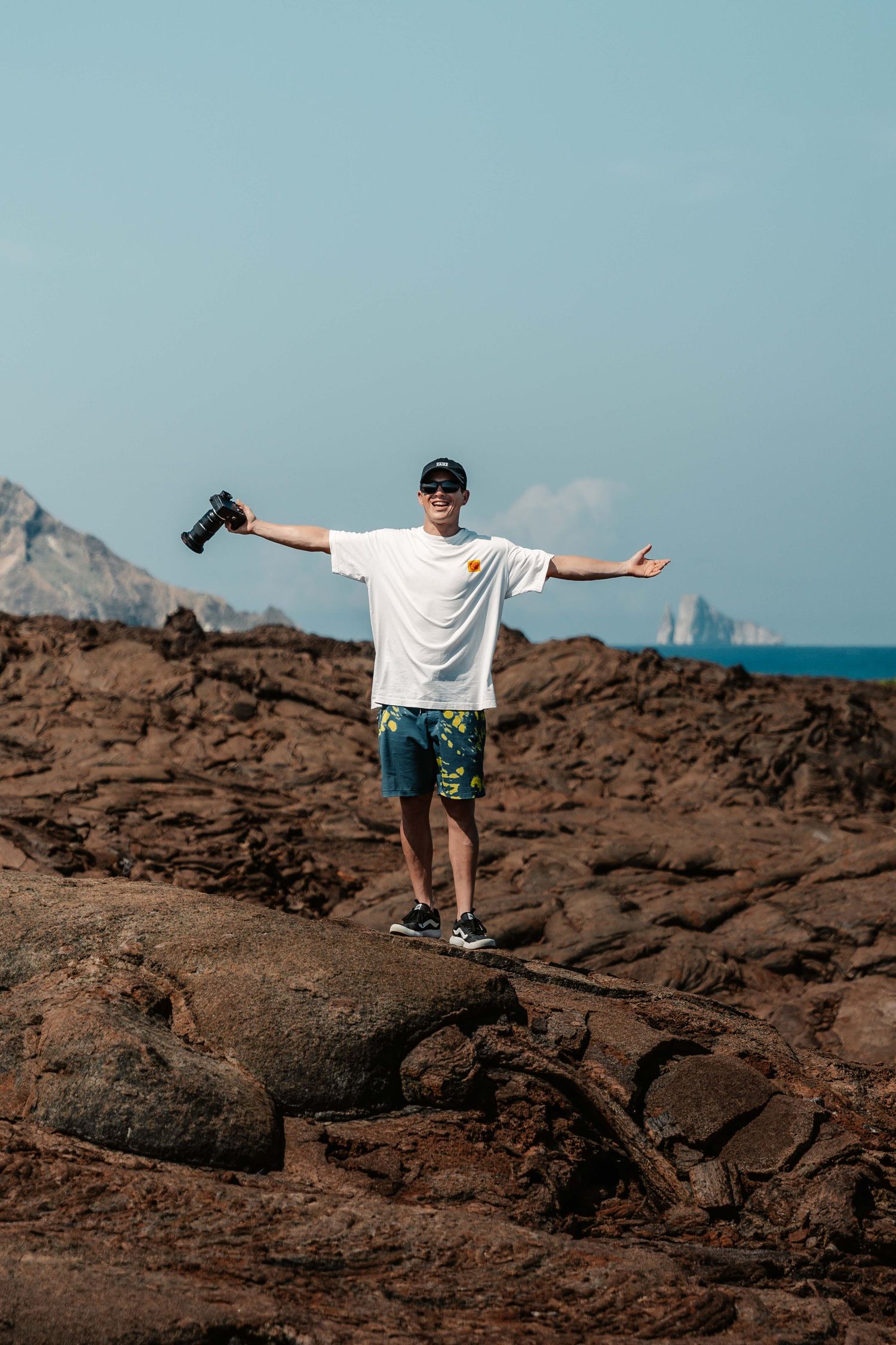 Person stands with arms outstretched on volcanic rocks overlooking ocean vista.