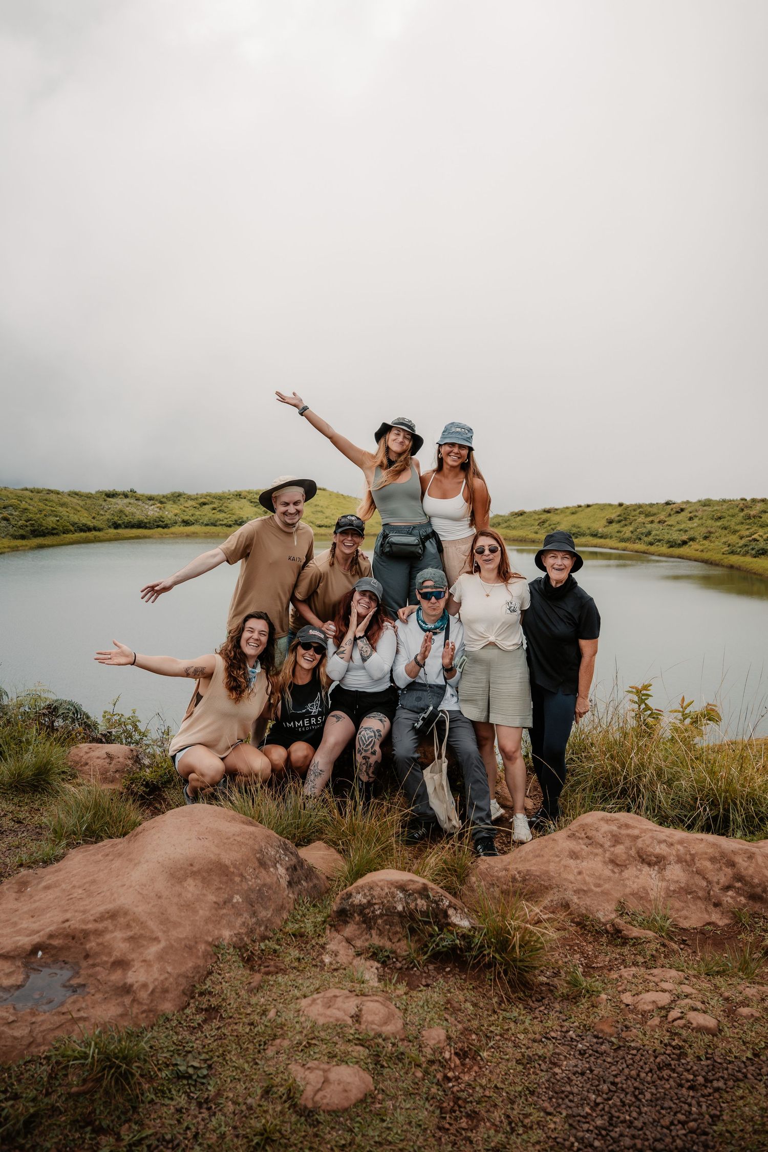 Group of women posing together on rocky terrain near a scenic lake during an outdoor hiking adventure.