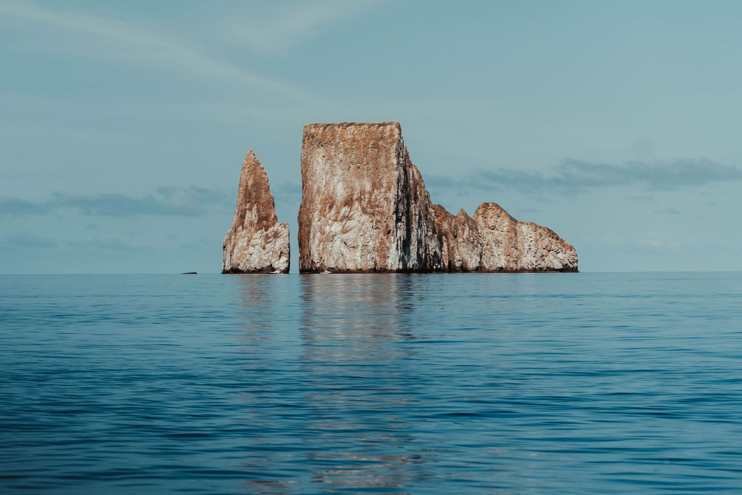 Dramatic view of Kicker Rock formation rising from blue ocean waters near the Galapagos Islands at sunset.