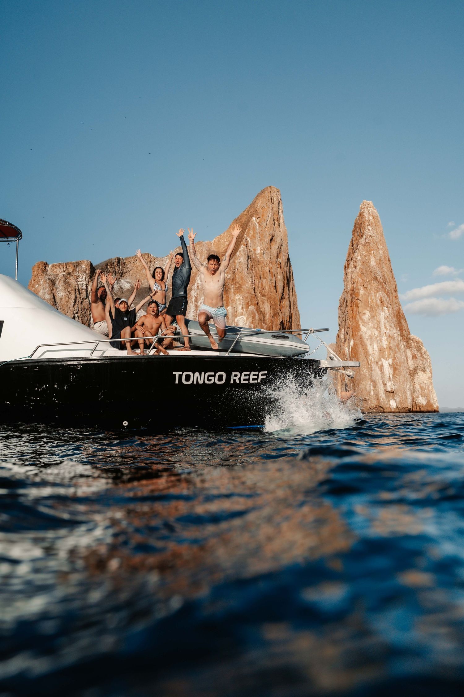Dramatic coastal rock formations rise from blue waters with a boat visible in the distance.