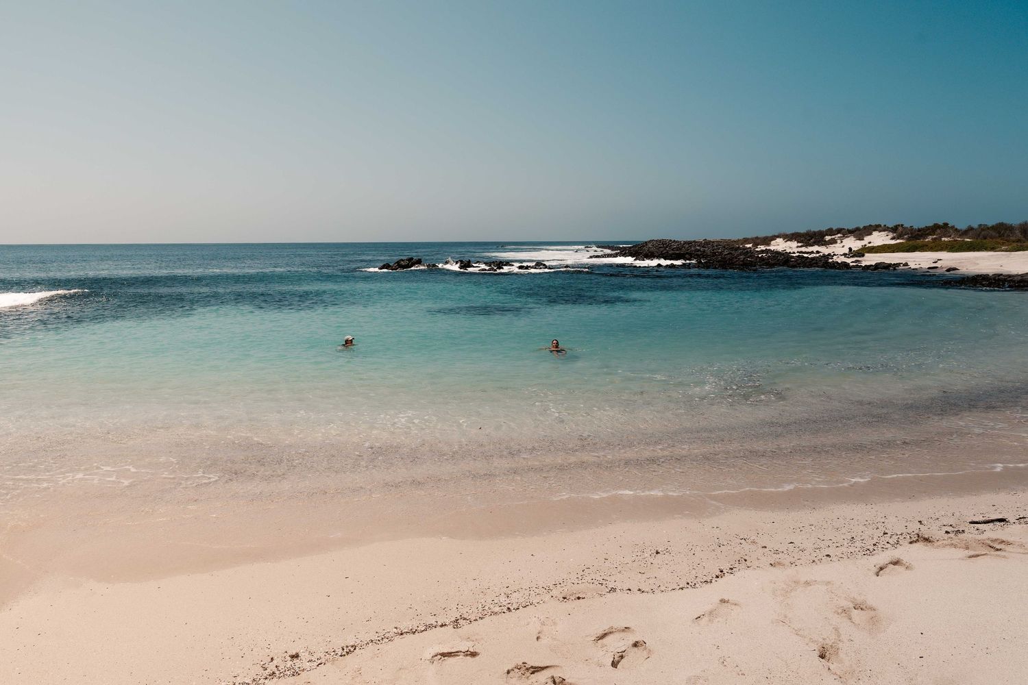 Tranquil beach scene with crystal clear turquoise waters and black volcanic rocks along the shoreline.